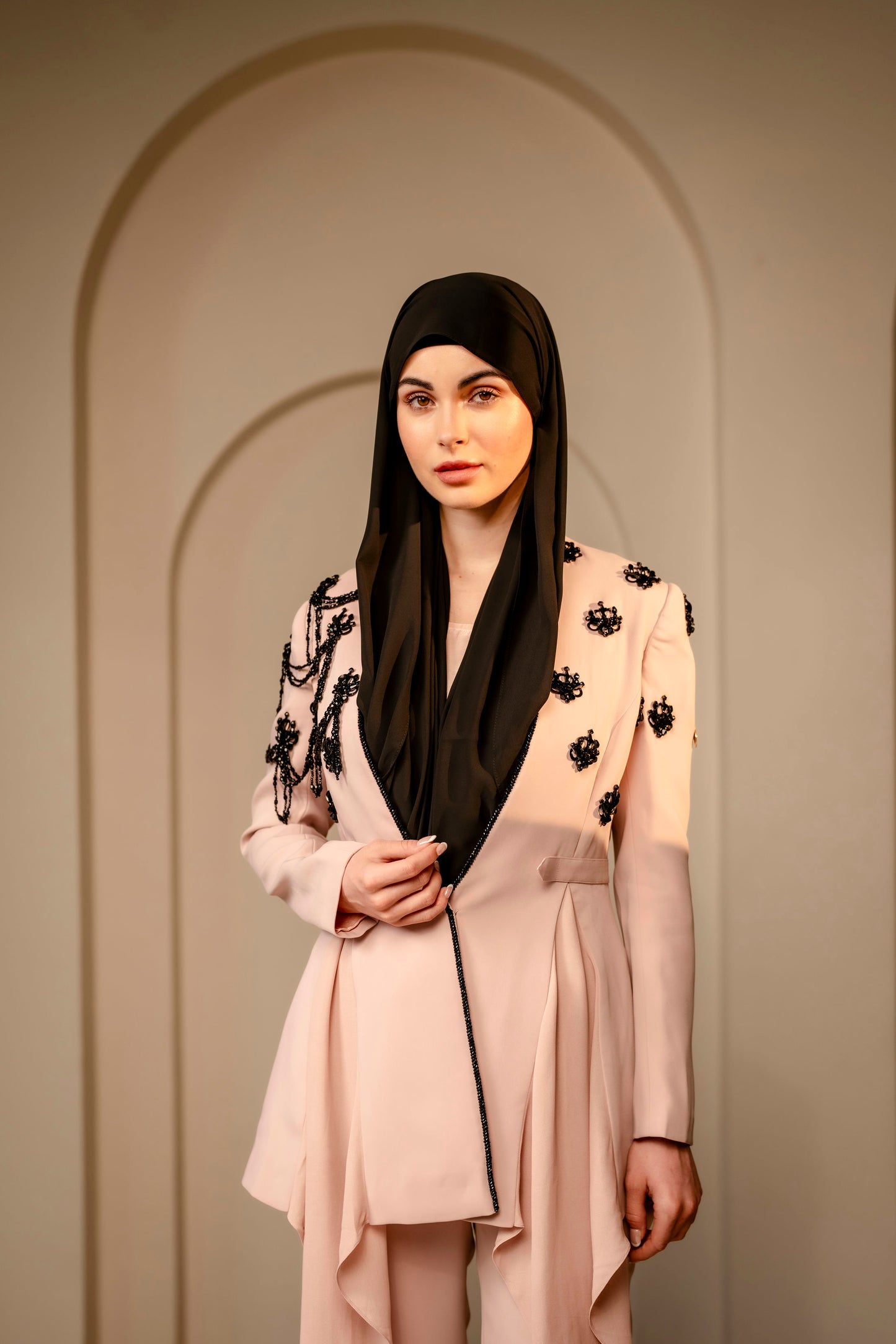 Woman wearing a beige outfit with black floral details against a neutral background