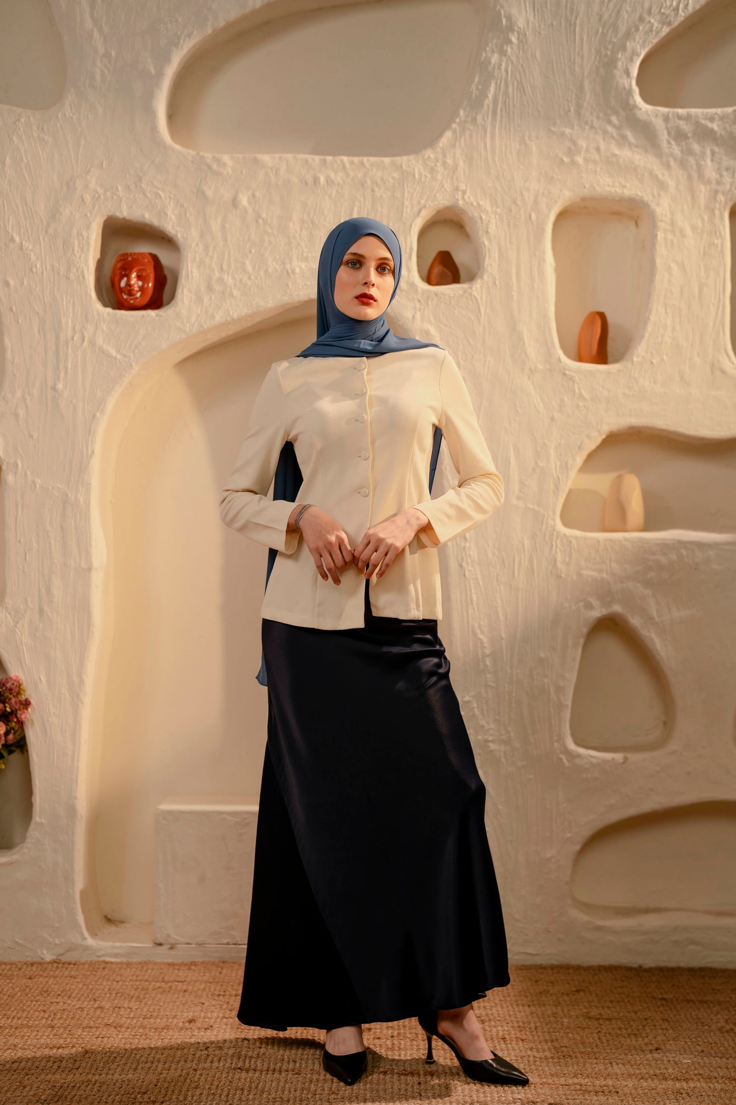 Woman wearing a white blouse and dark skirt with a blue hijab in front of an abstract wall - Whispering Blue