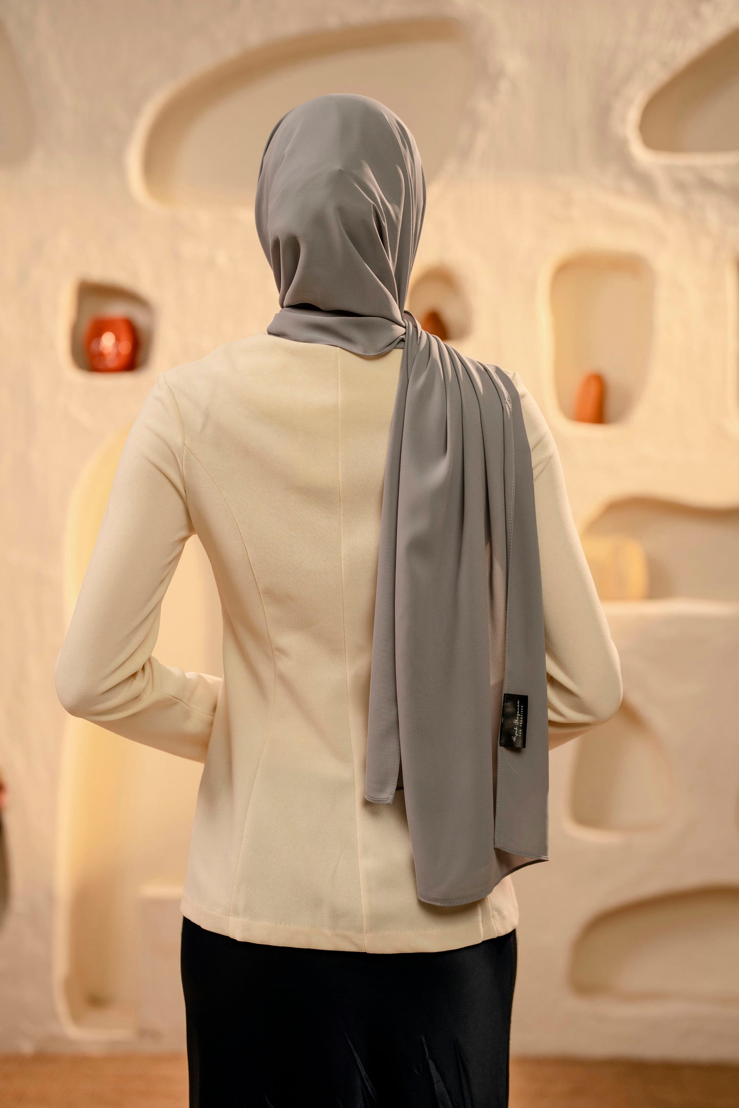 Person wearing a gray hijab and beige top against an abstract wall.