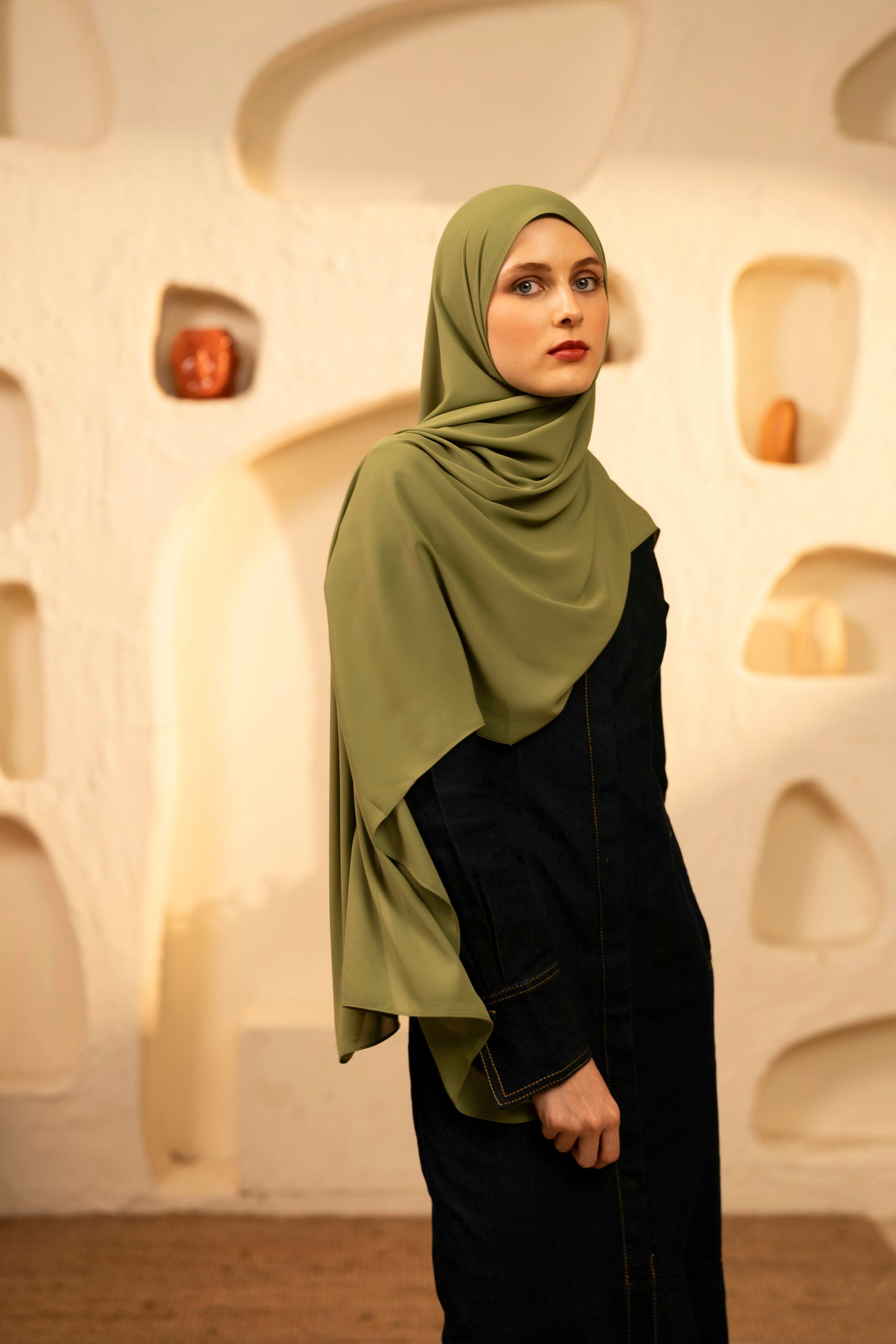 Woman wearing a green hijab and dark outfit in an artistic setting - olive green