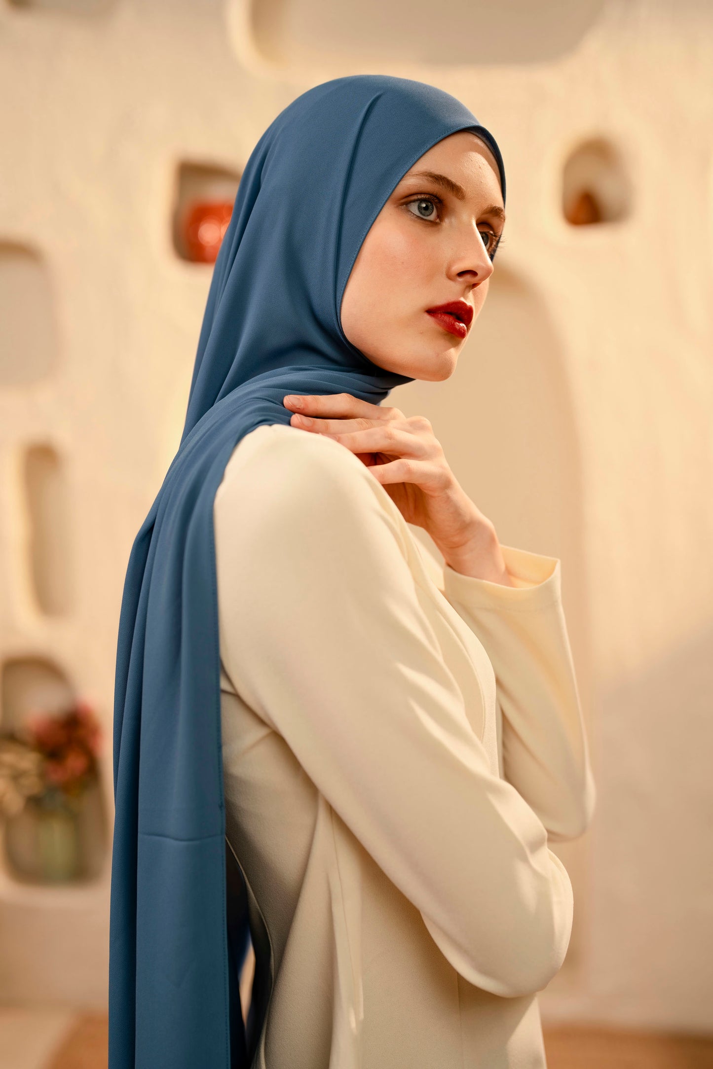 Woman wearing a blue hijab and white outfit in a softly blurred indoor setting - whispering blue