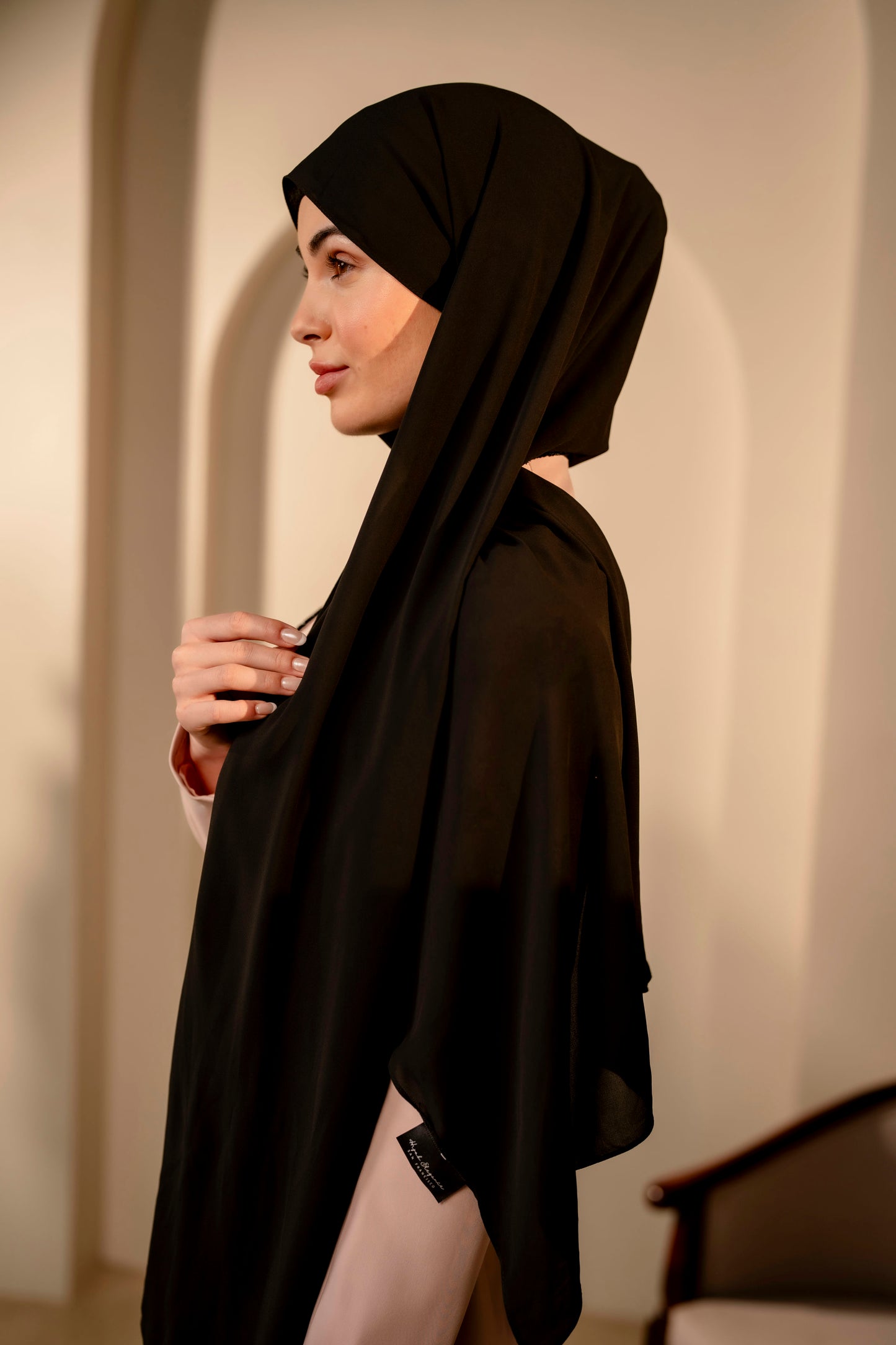 Woman wearing a black hijab and black outfit against a neutral background