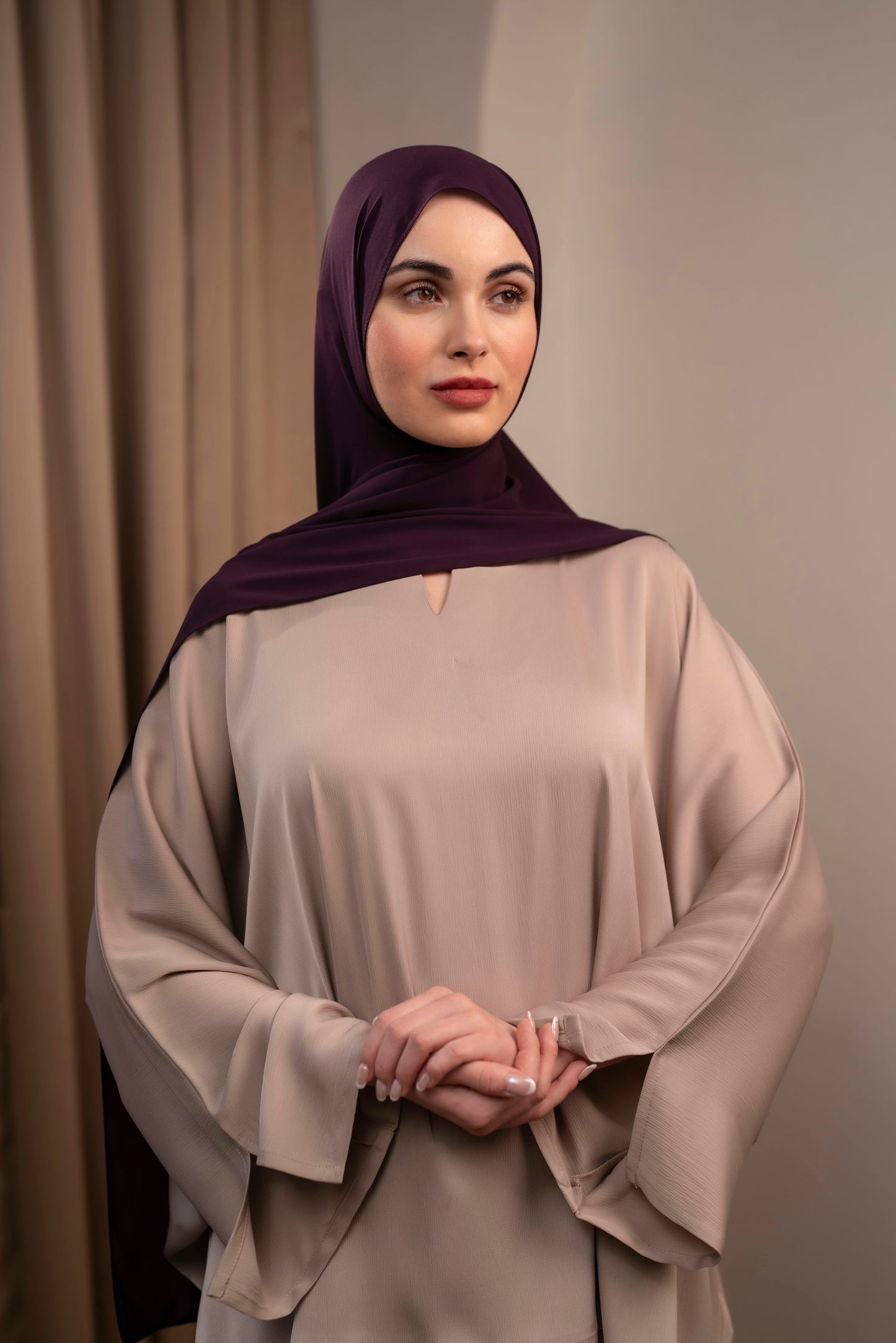 Woman wearing a beige dress and dark hijab against a neutral background - Plum