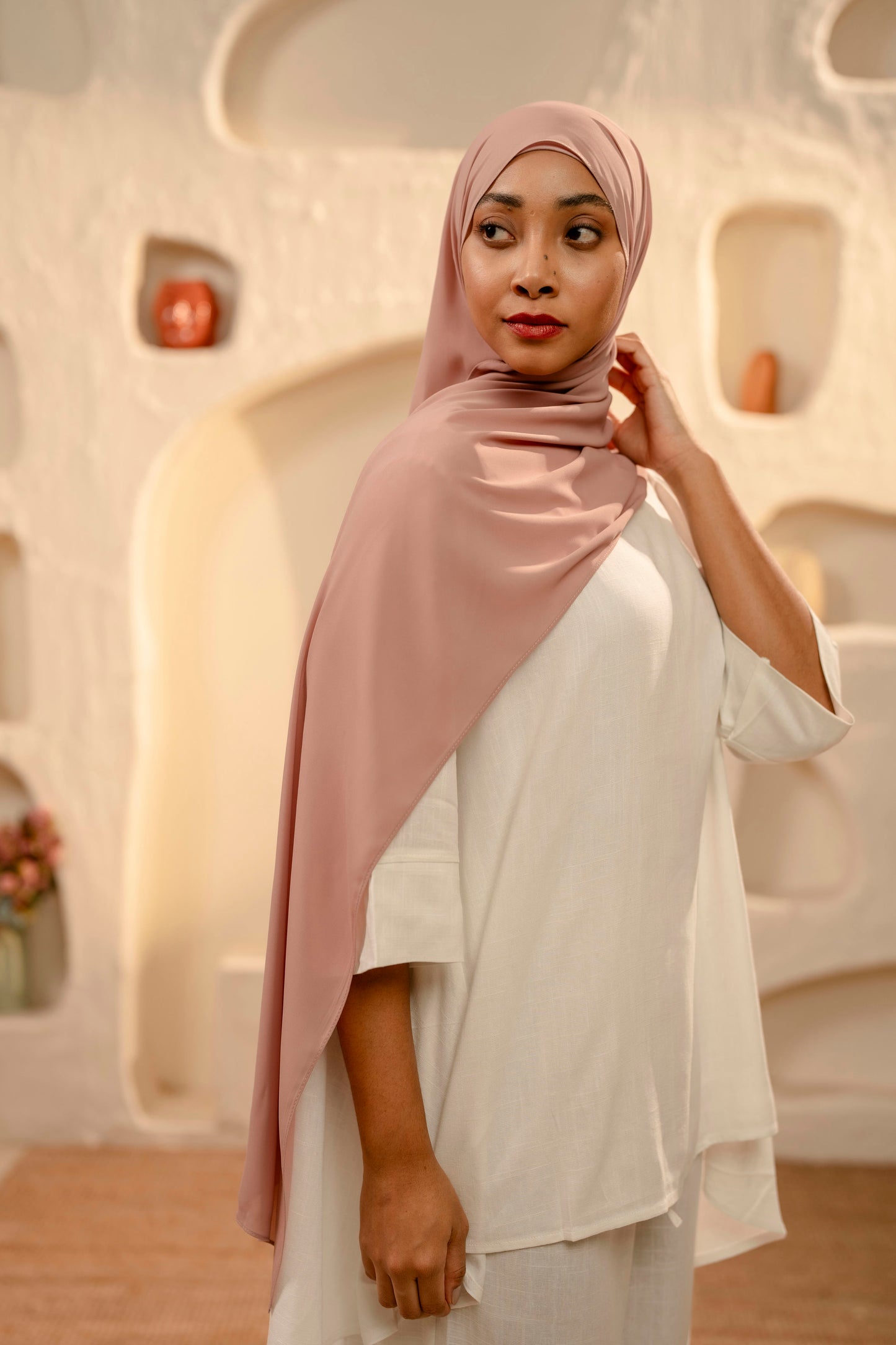 Woman wearing a pink hijab and white outfit in a modern architectural setting - dusty pink