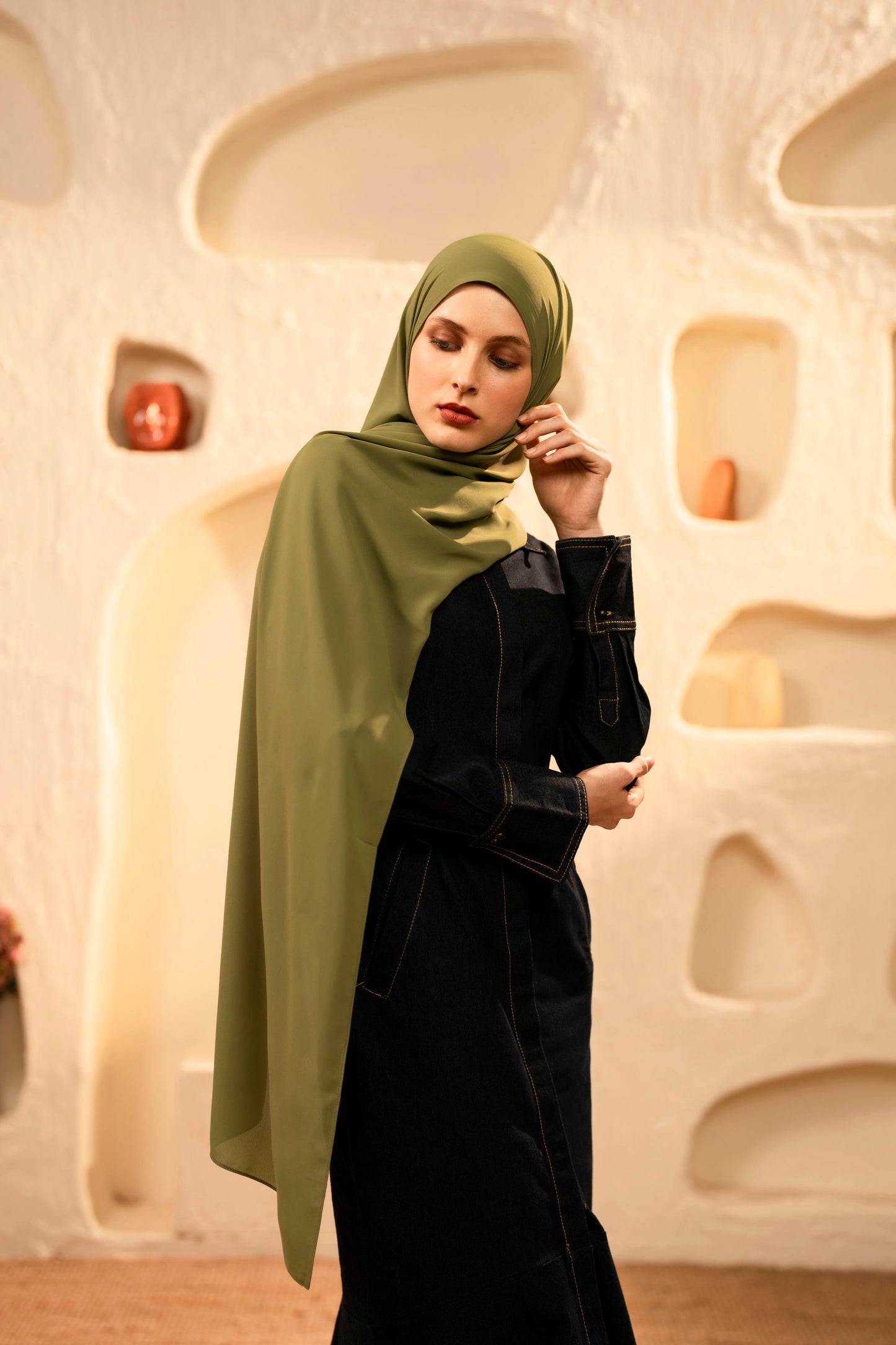 Woman wearing a green hijab and dark outfit against an abstract beige wall - Olive green