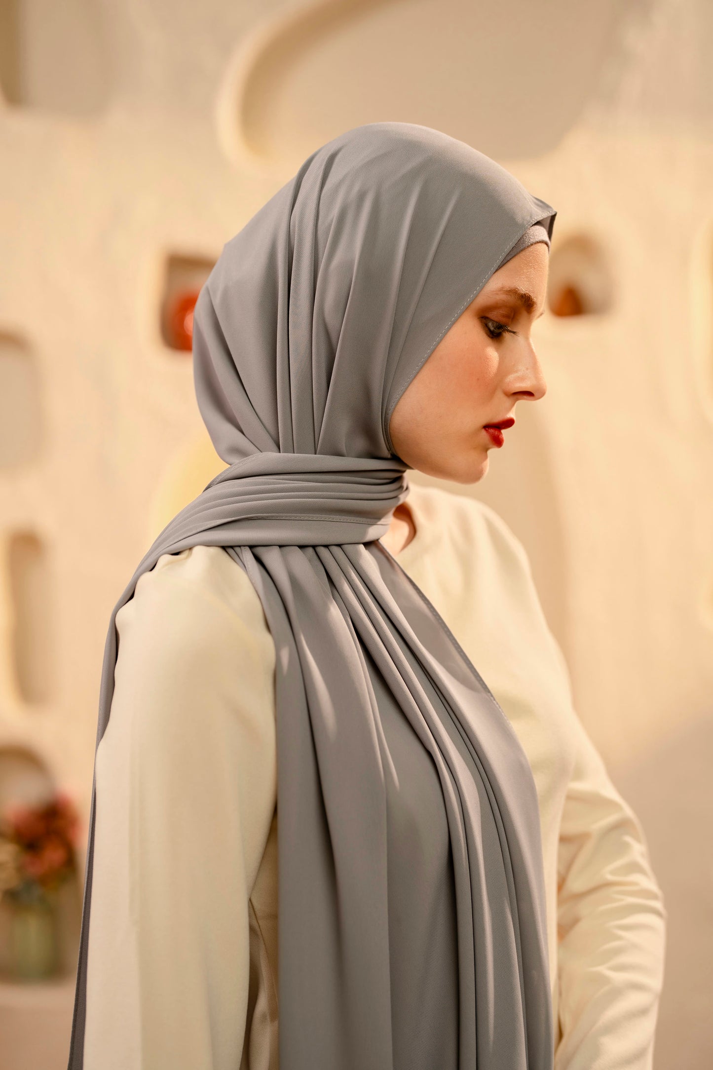 Woman wearing a gray hijab with a blurred architectural background