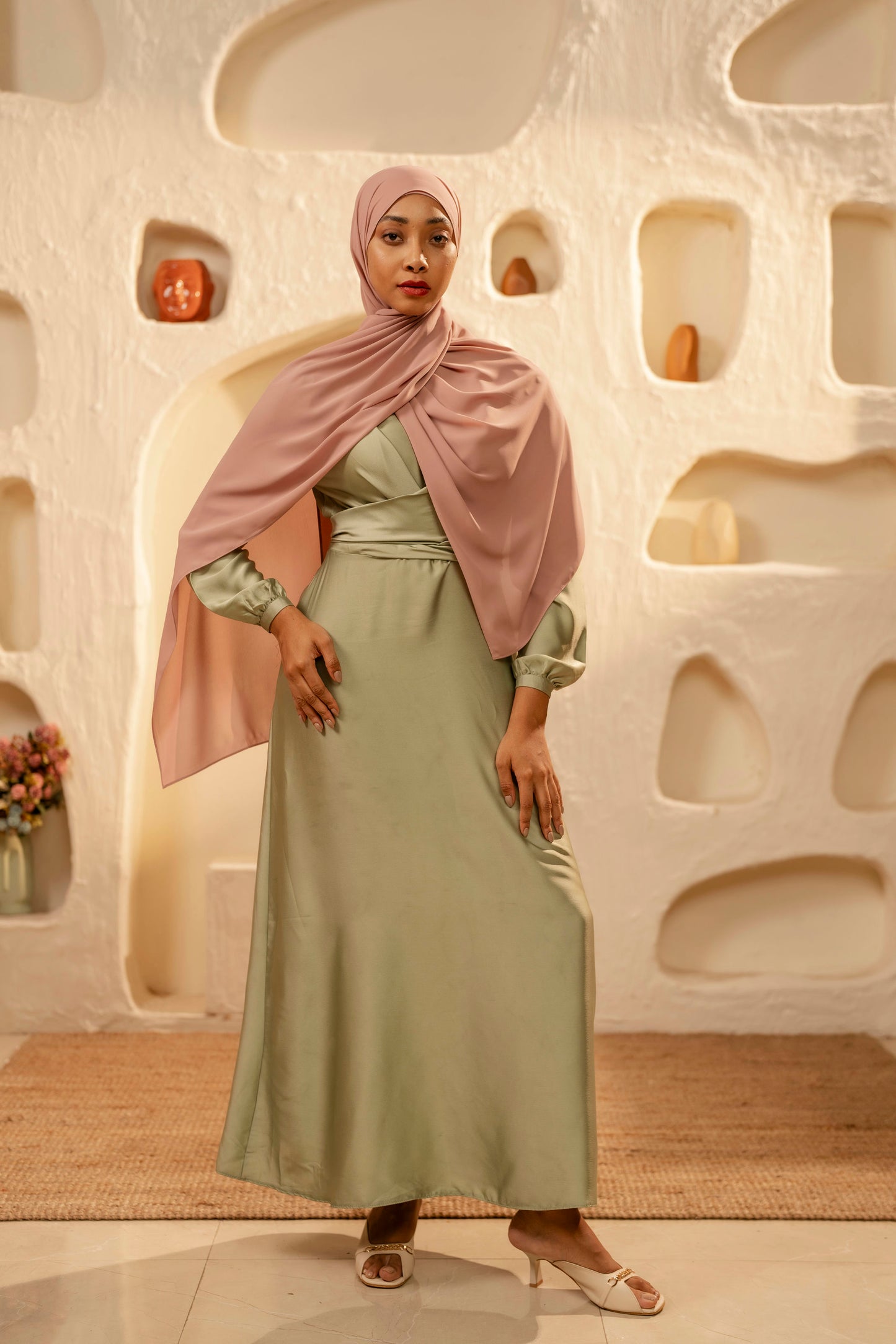 Woman in a green dress and pink hijab standing in front of an abstract wall - dusty pink