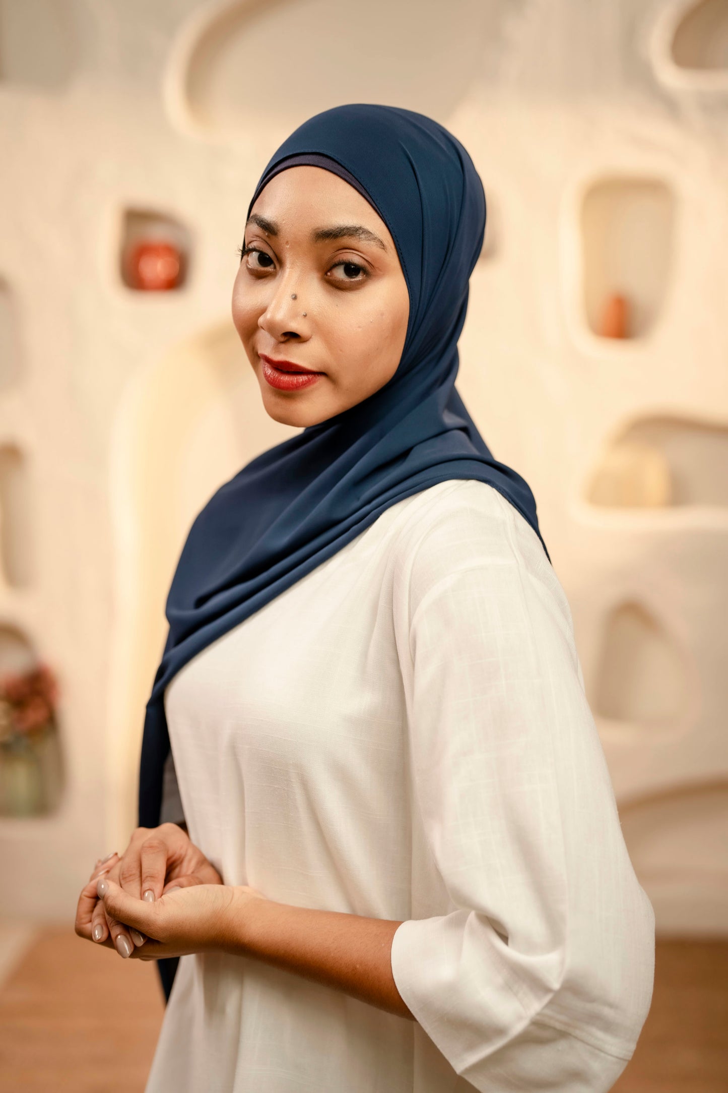 Woman wearing a navy hijab and white shirt in an indoor setting