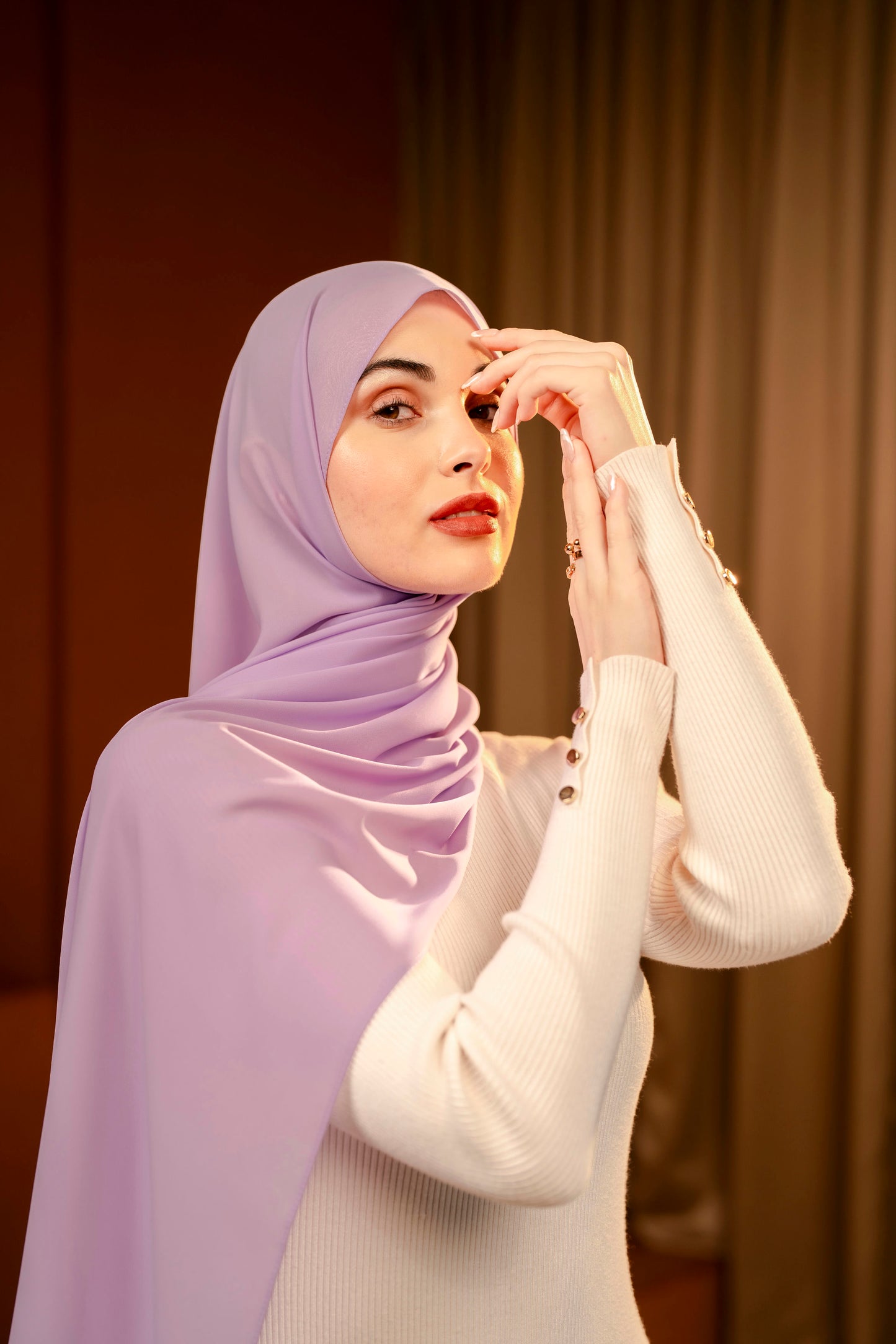 Woman wearing a light purple hijab and white sweater against a dark sandy curtain background - Lavender