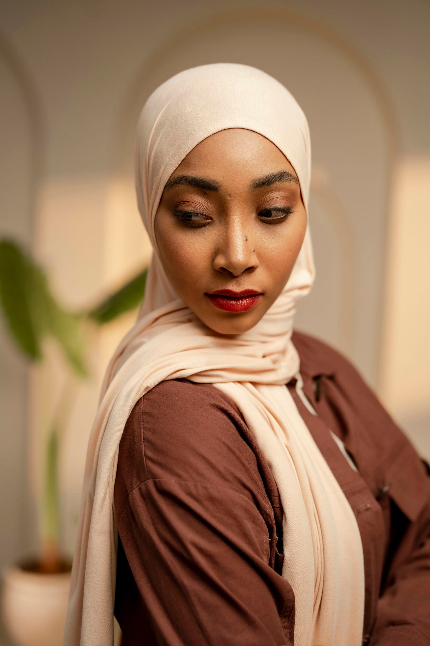 Woman wearing a beige hijab and brown top in an indoor setting