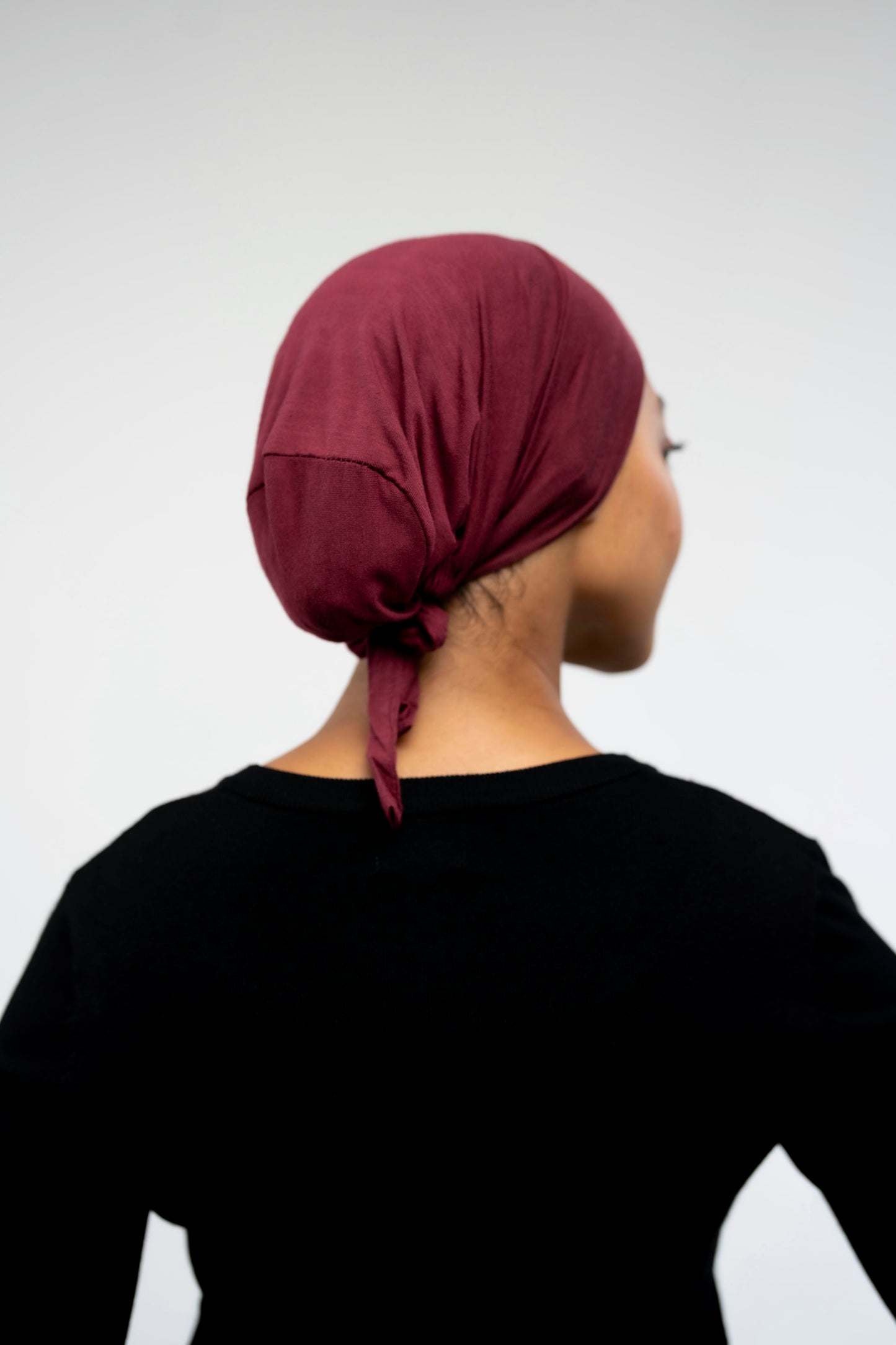 Person wearing a burgundy headscarf on a light background - maroon