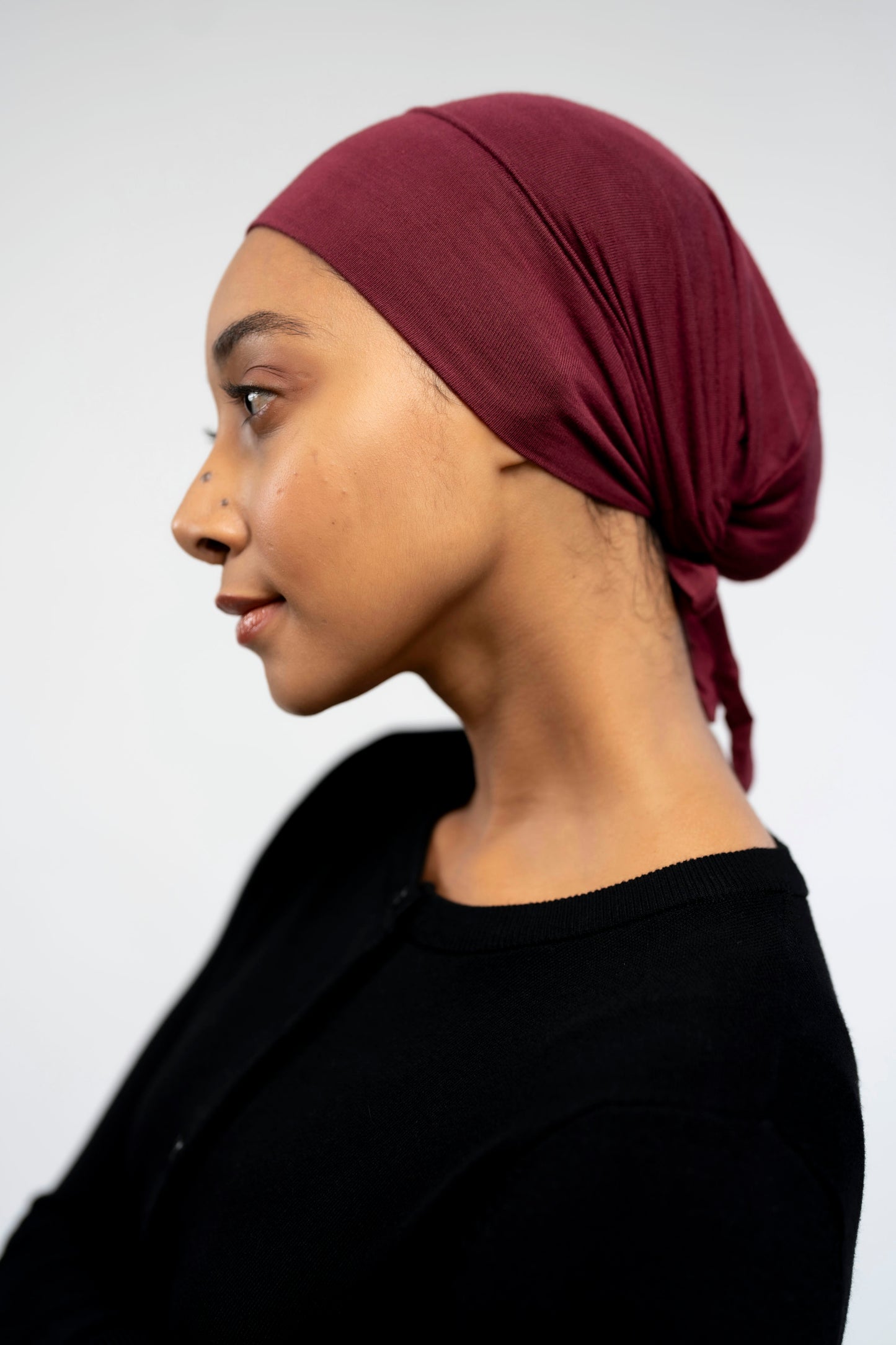 Woman wearing a maroon headscarf against a light background