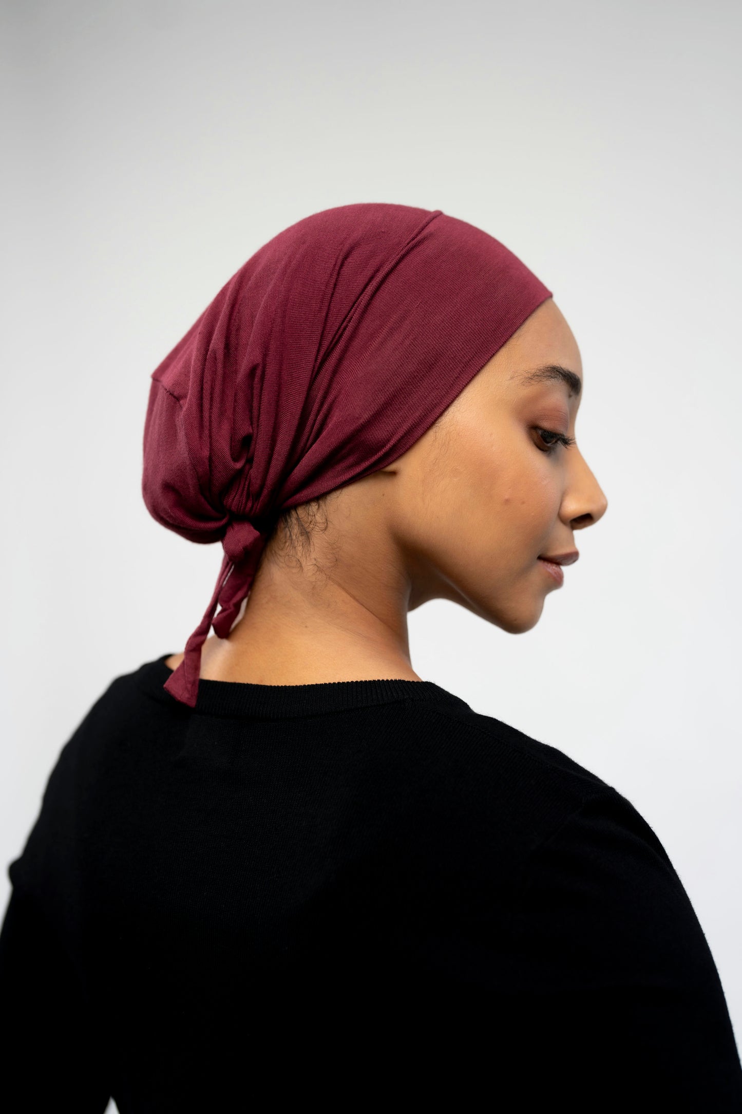 Woman wearing a maroon headscarf on a light background
