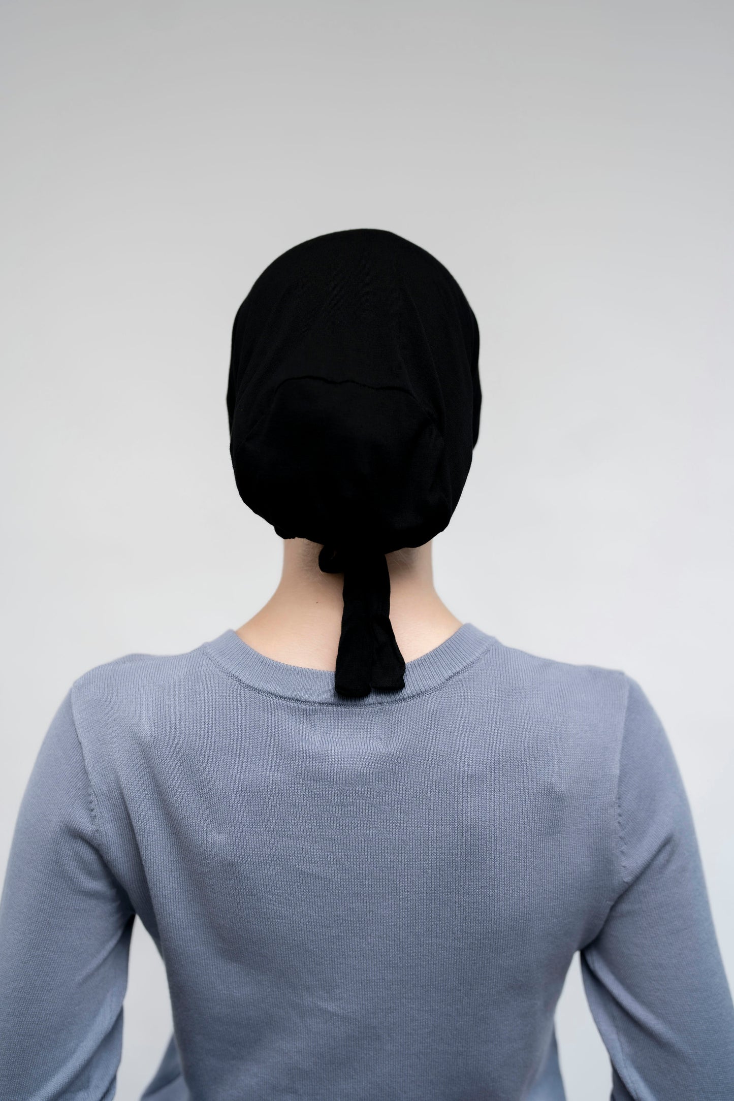 Person wearing a black headscarf on a plain background