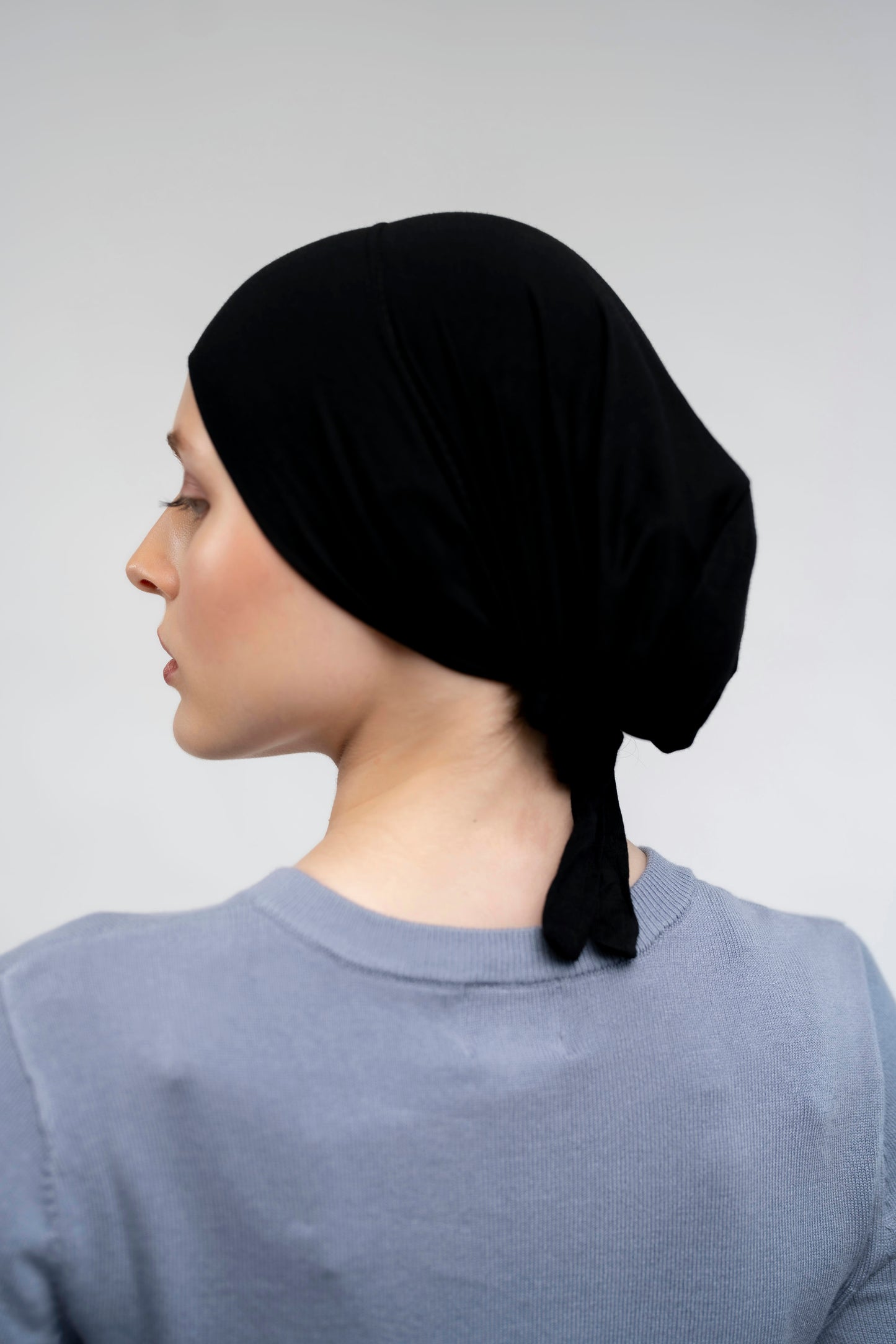 Woman wearing a black headscarf on a plain background