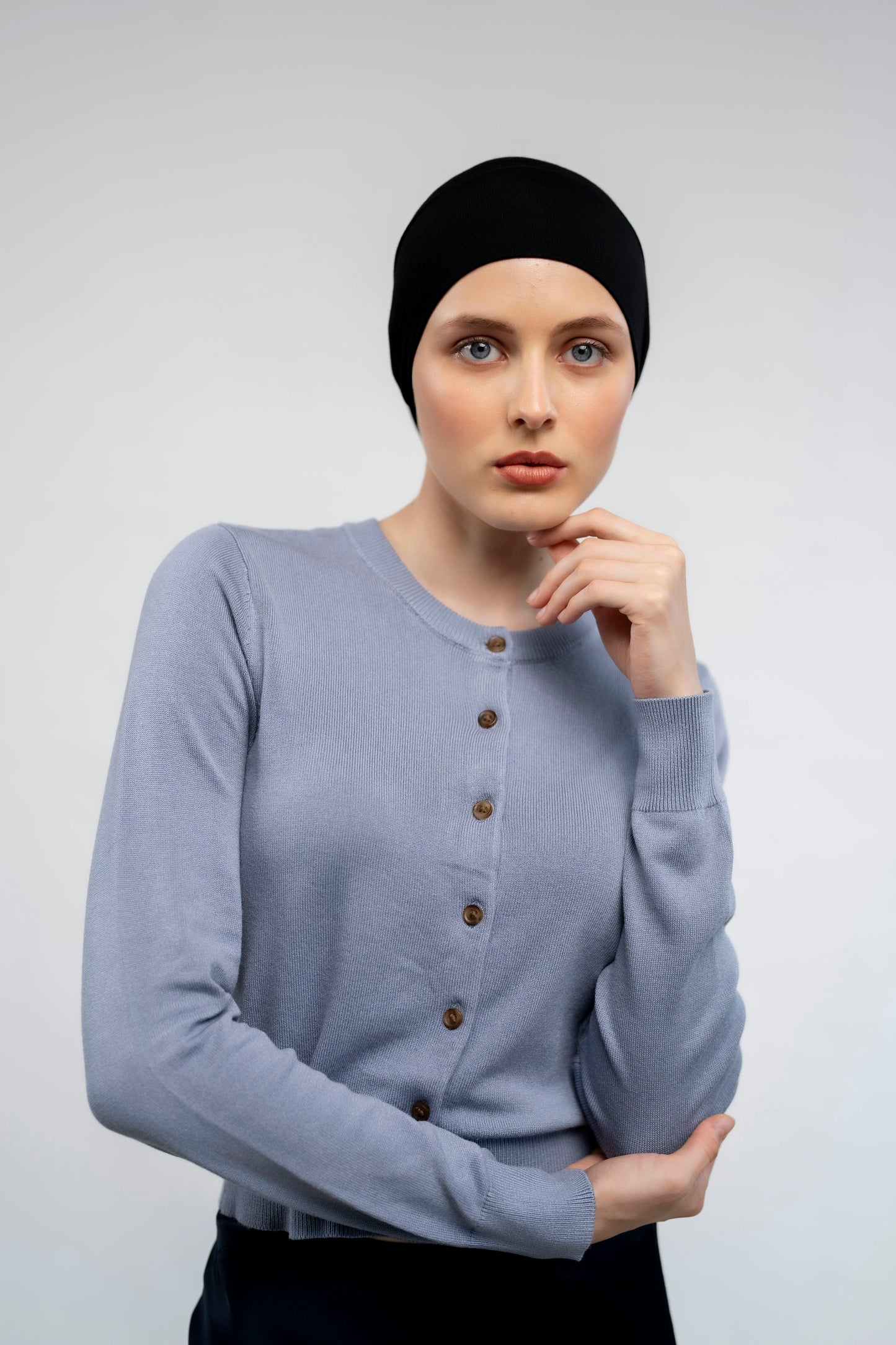 Woman wearing a black headscarf and light aqua sweater against a light background