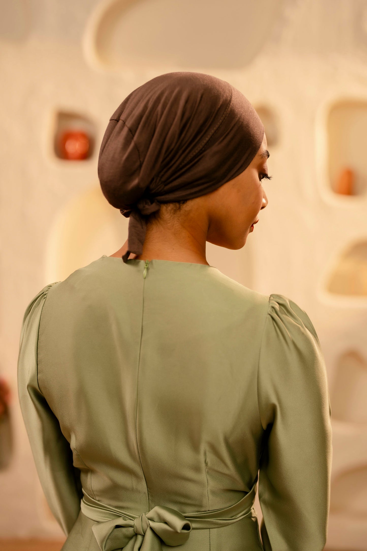 Woman wearing a mint dress with a coffee brown headscarf in a softly blurred indoor setting