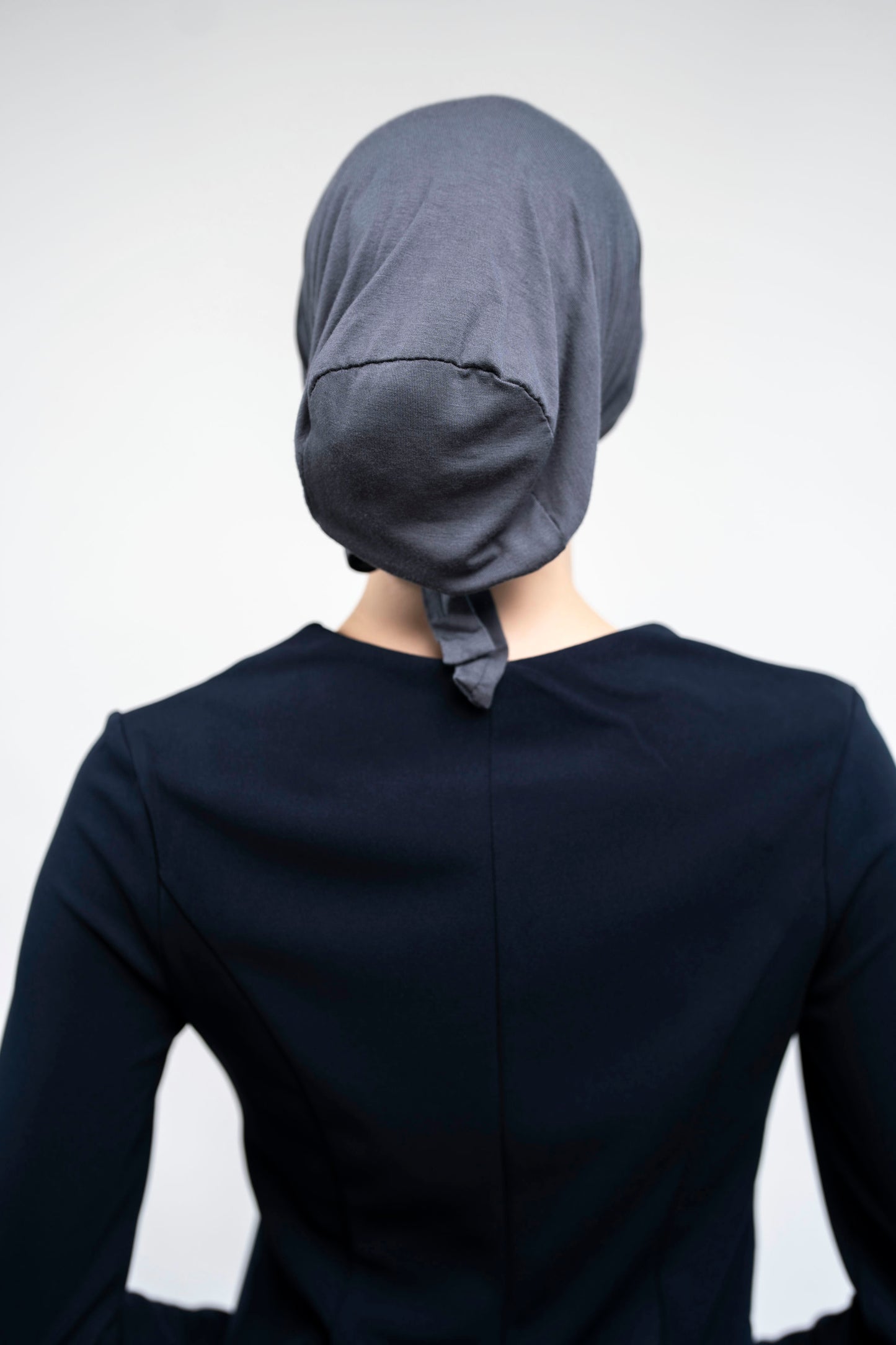 Person wearing a dark gray hijab and dark outfit against a light gray background