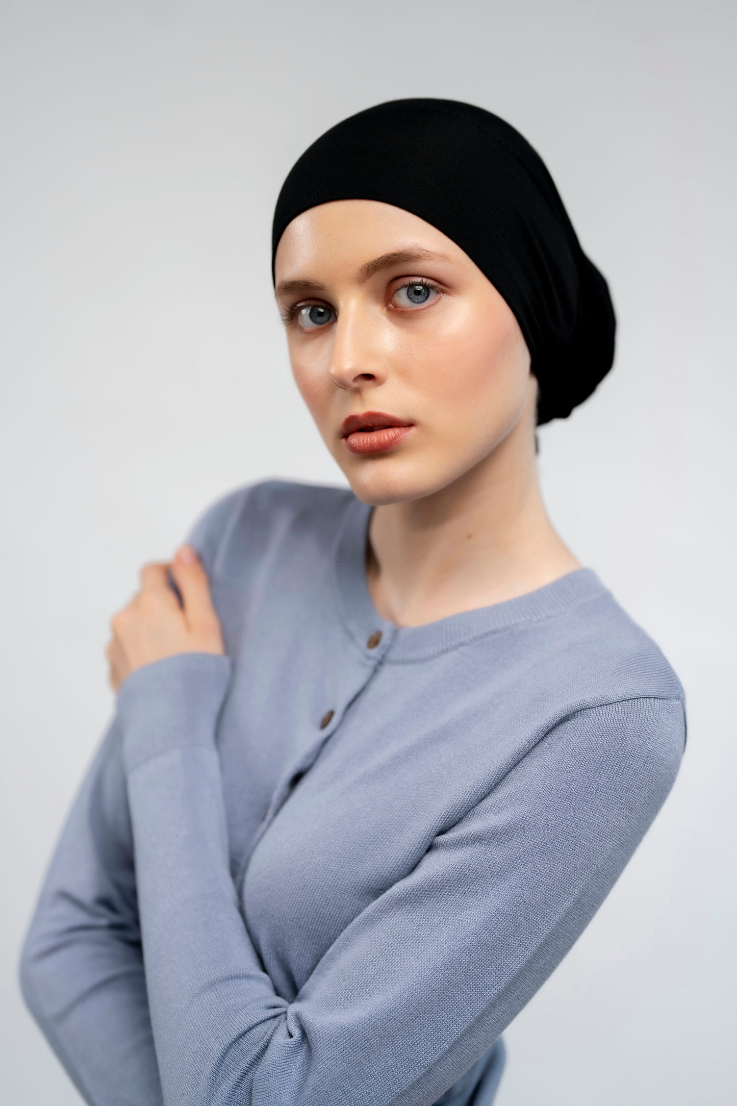 Woman wearing a black headscarf and light aqua sweater against a light background