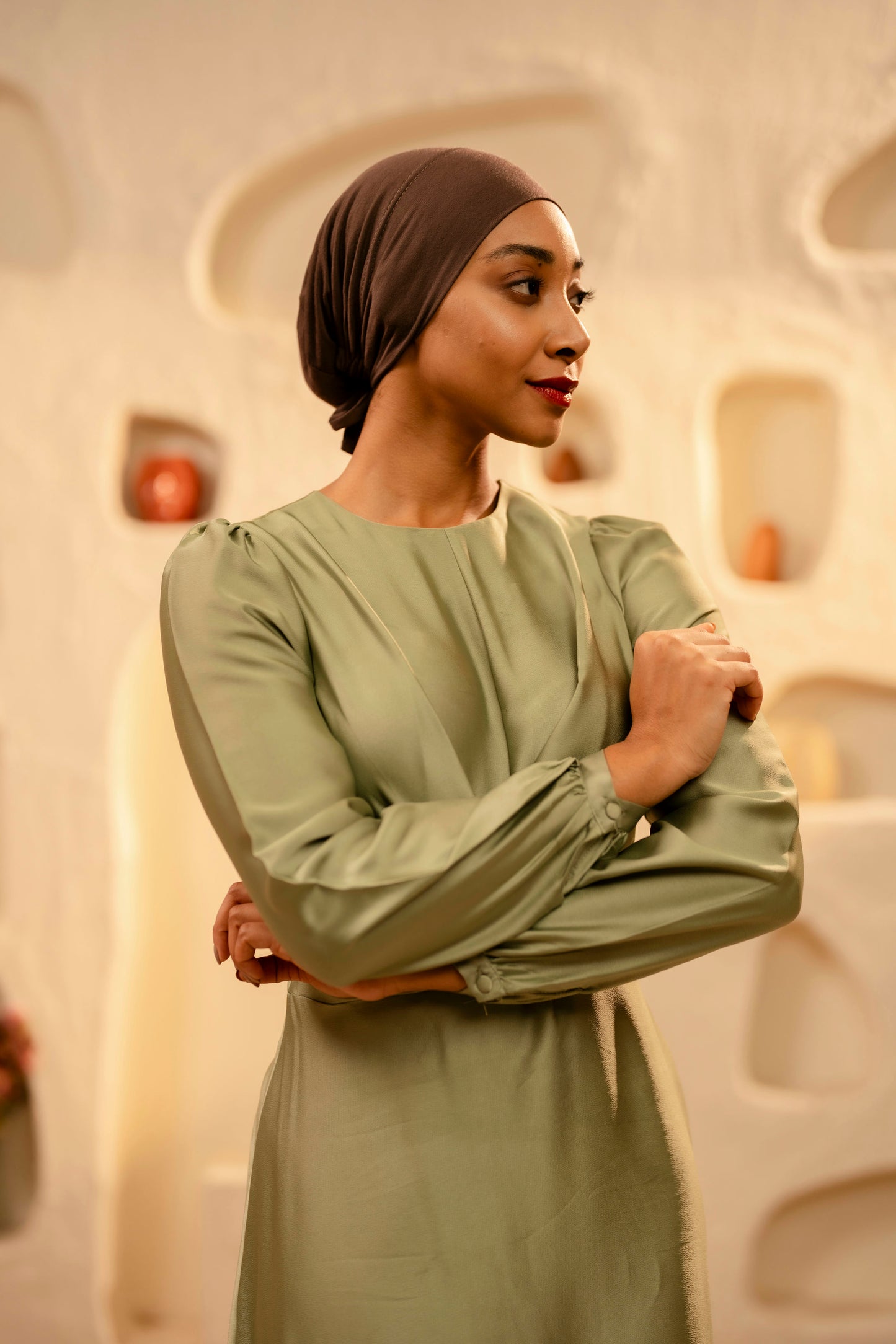 Woman in a mint dress with a coffee brown headscarf standing against an abstract wall.