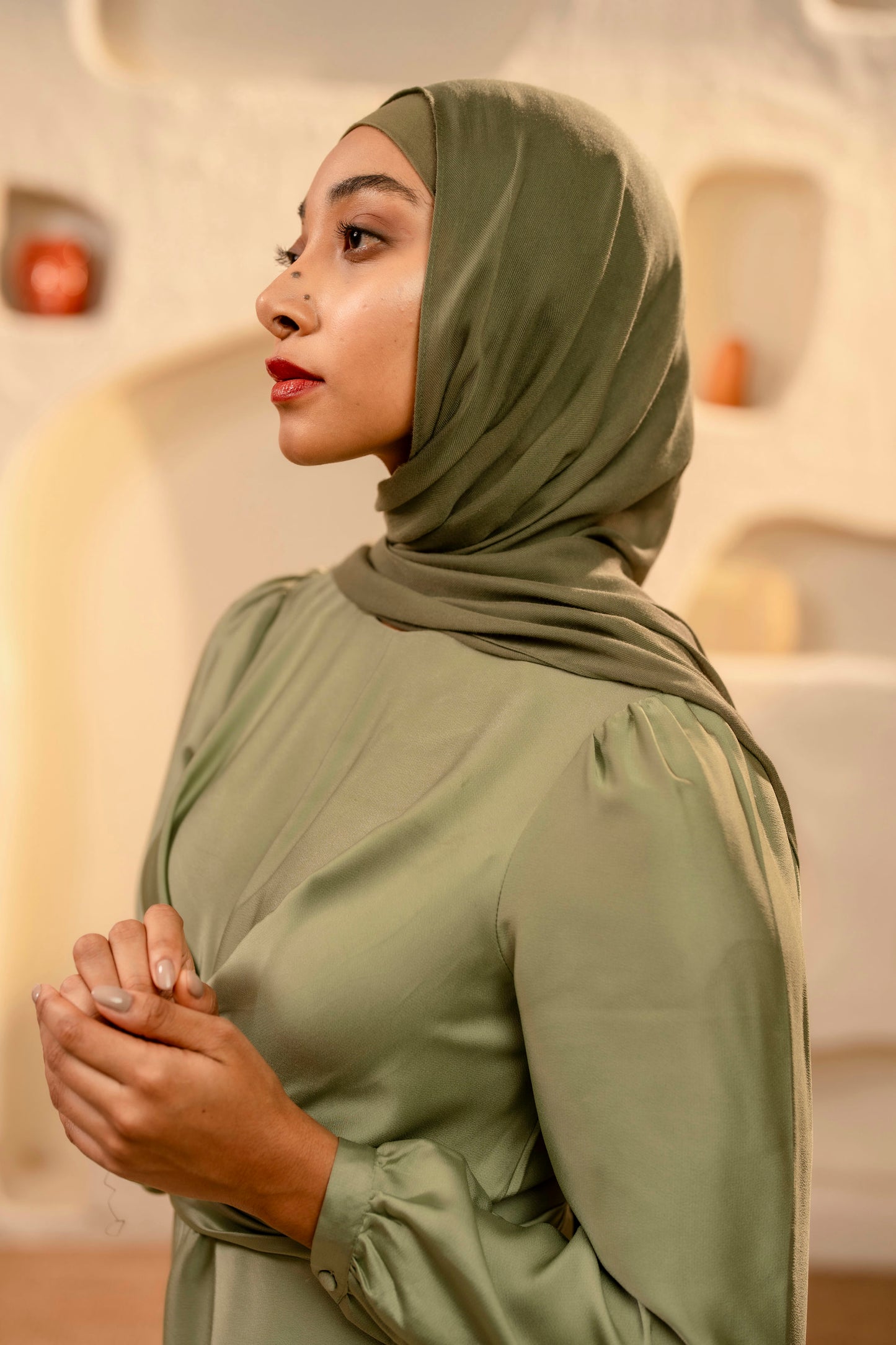 Woman wearing a olive green hijab and dress in an indoor setting
