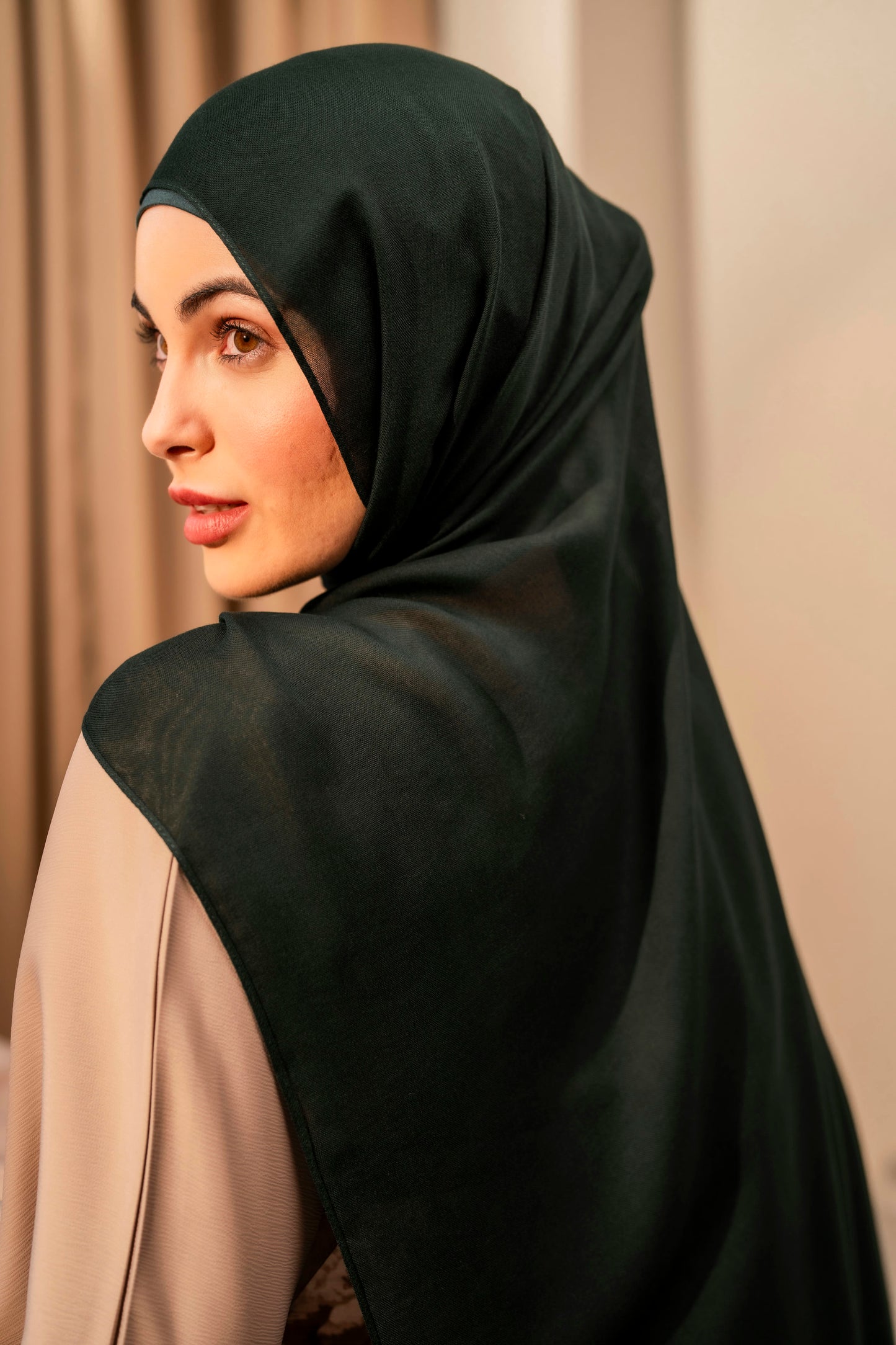 Woman wearing a forest green hijab with a beige background
