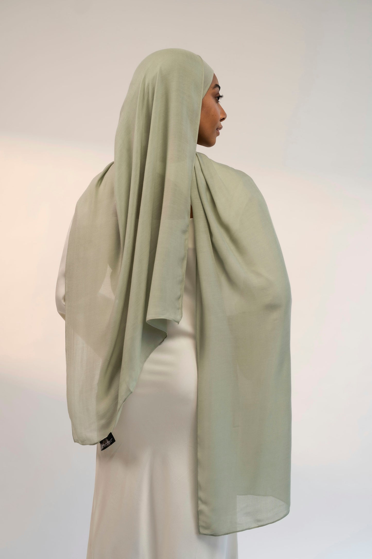 Person wearing a light green headscarf and white outfit against a plain background