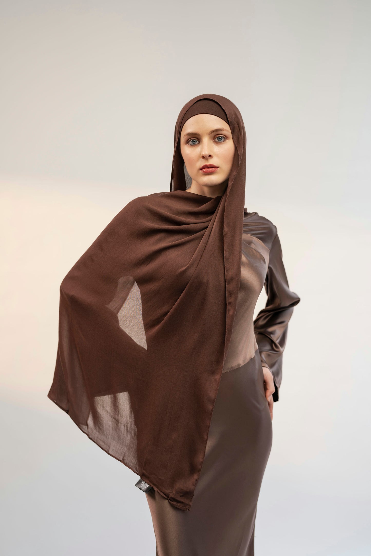 Woman wearing a brown hijab and dress against a plain background - coffee brown