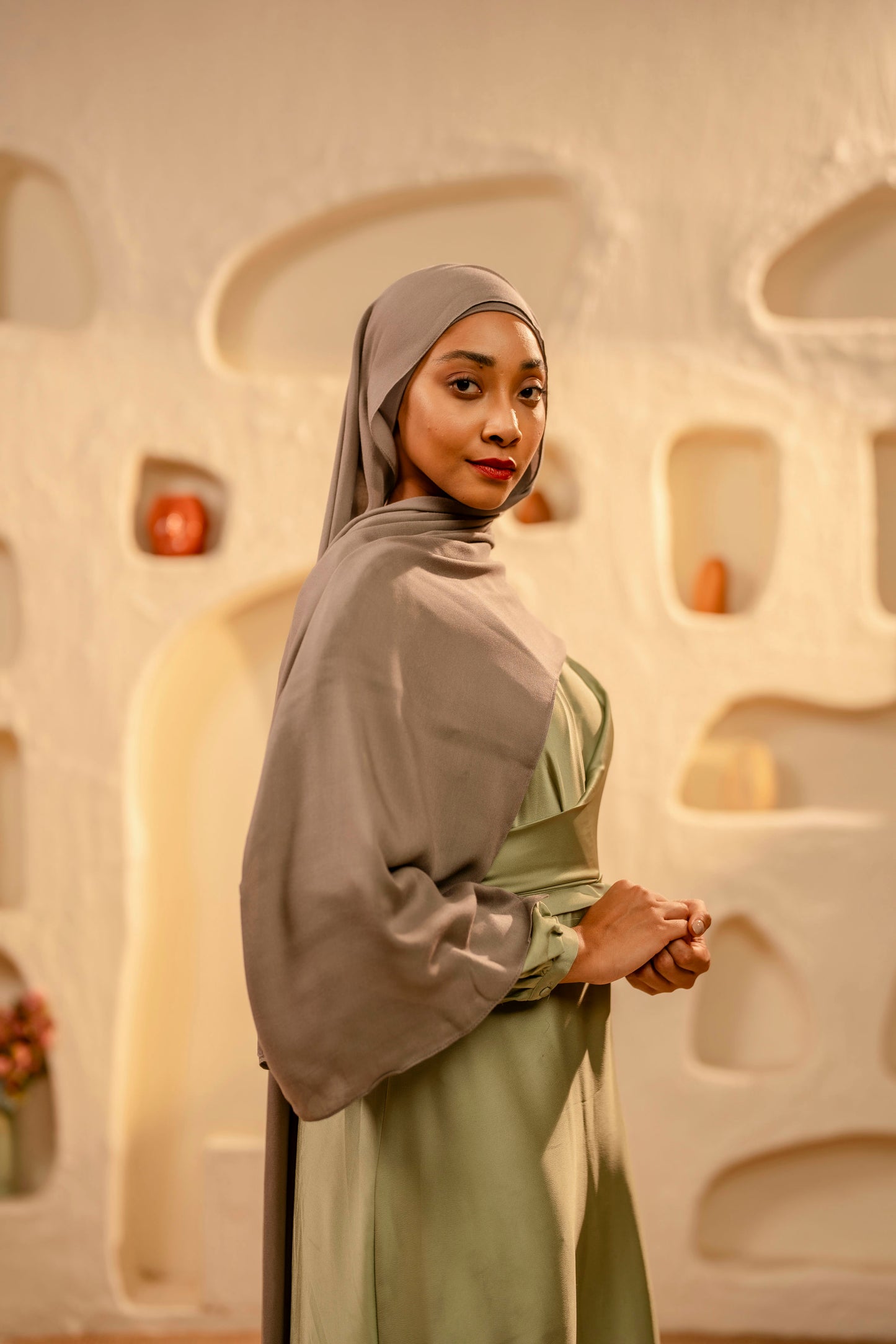Woman wearing a hijab and green outfit in front of an abstract wall - khaki
