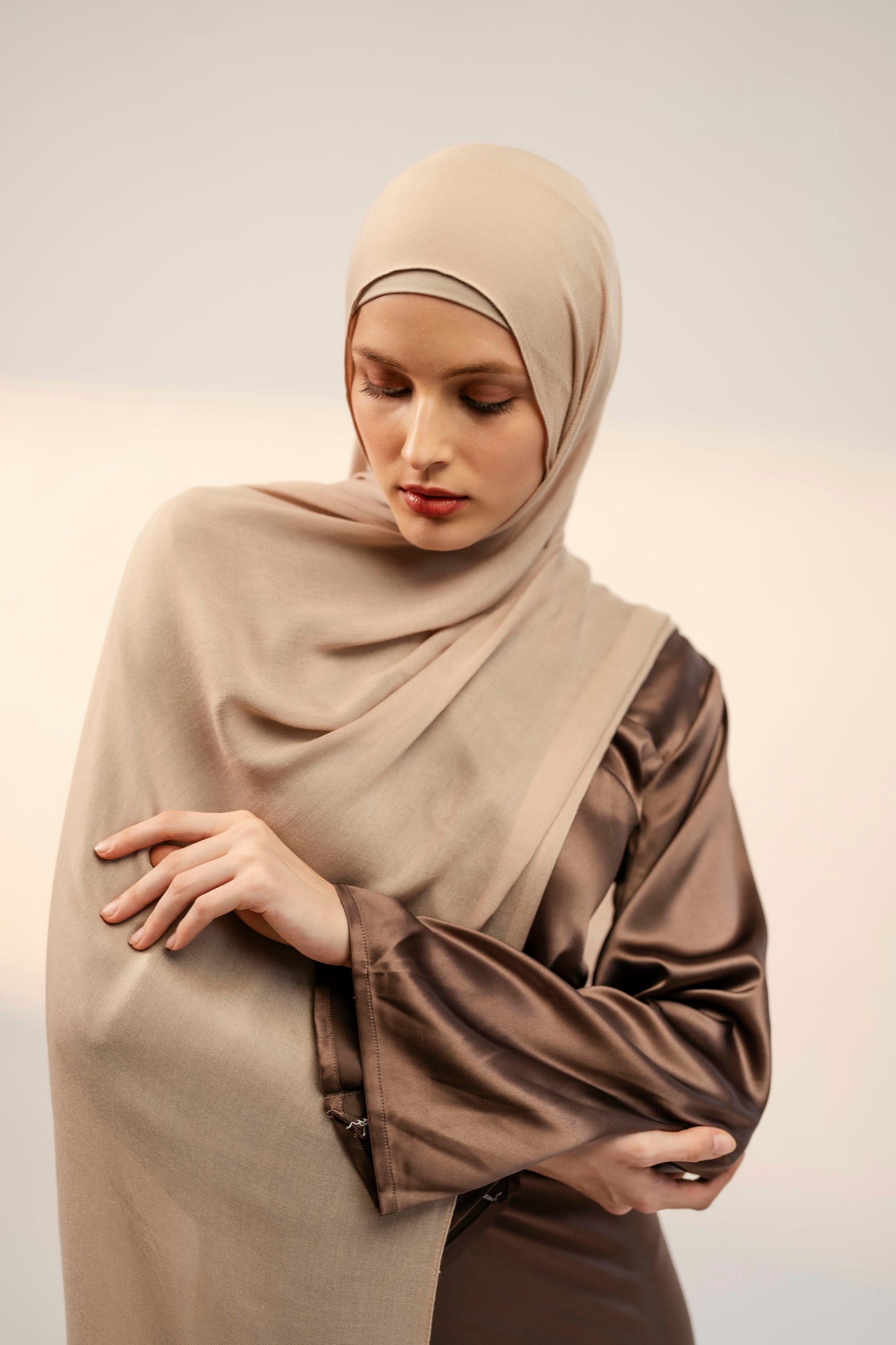 Woman wearing a beige hijab and brown outfit against a plain background - nude