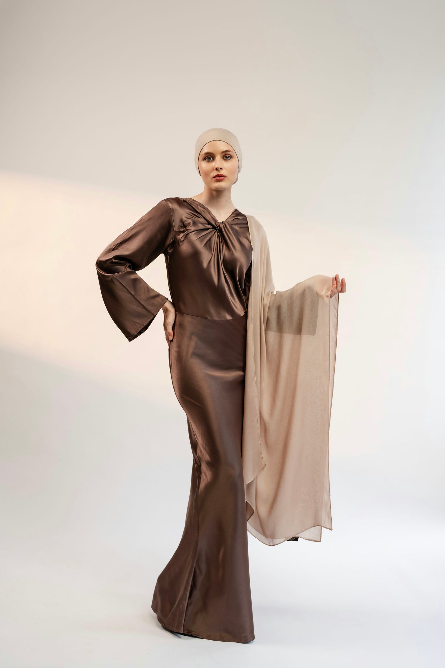 Woman wearing a brown satin dress with a beige hijab against a white background - nude color