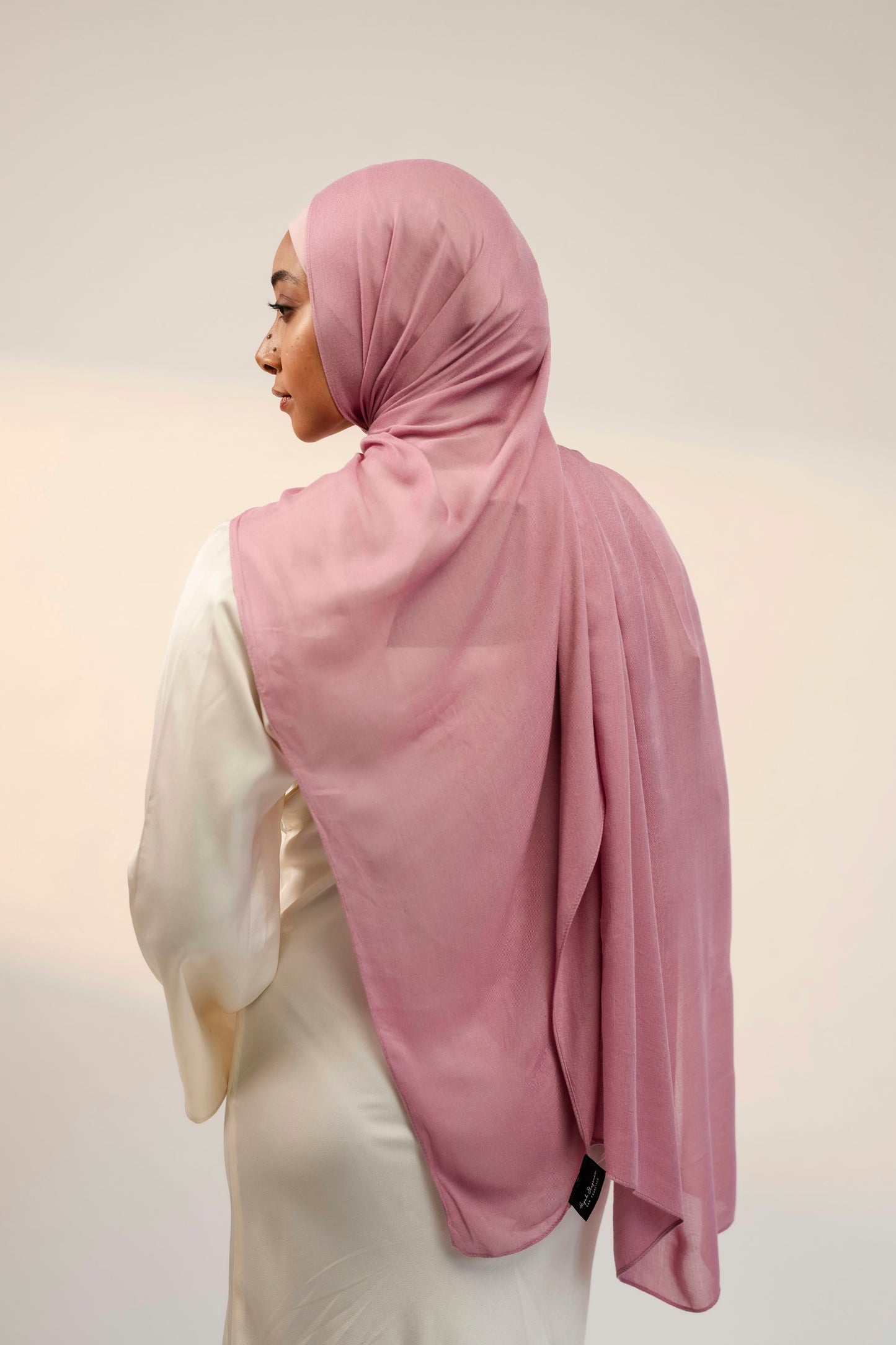 Person wearing a pink hijab and white outfit on a plain background - cherry blossom