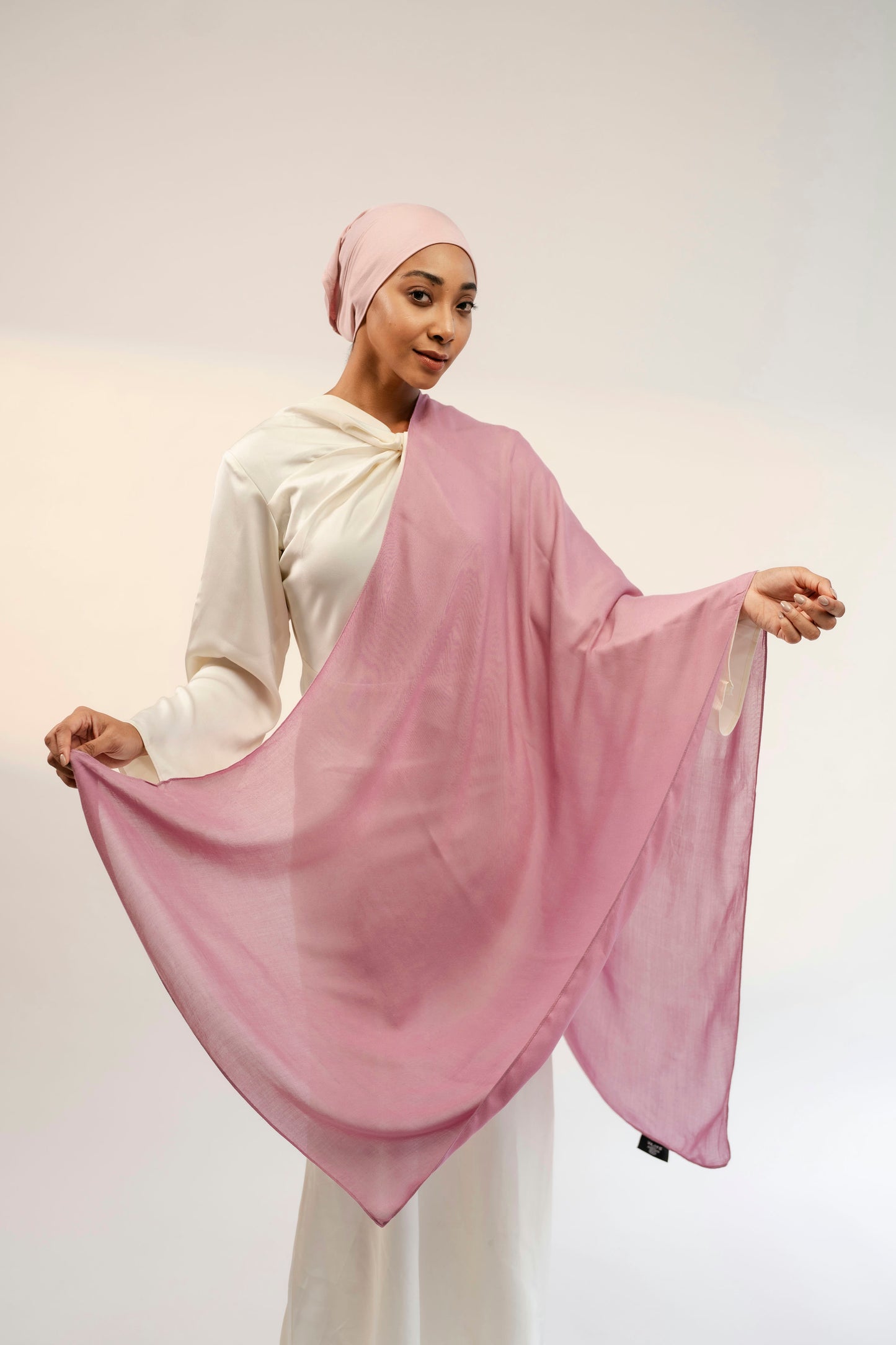 Woman wearing a pink hijab and white outfit against a plain background - cherry blossom