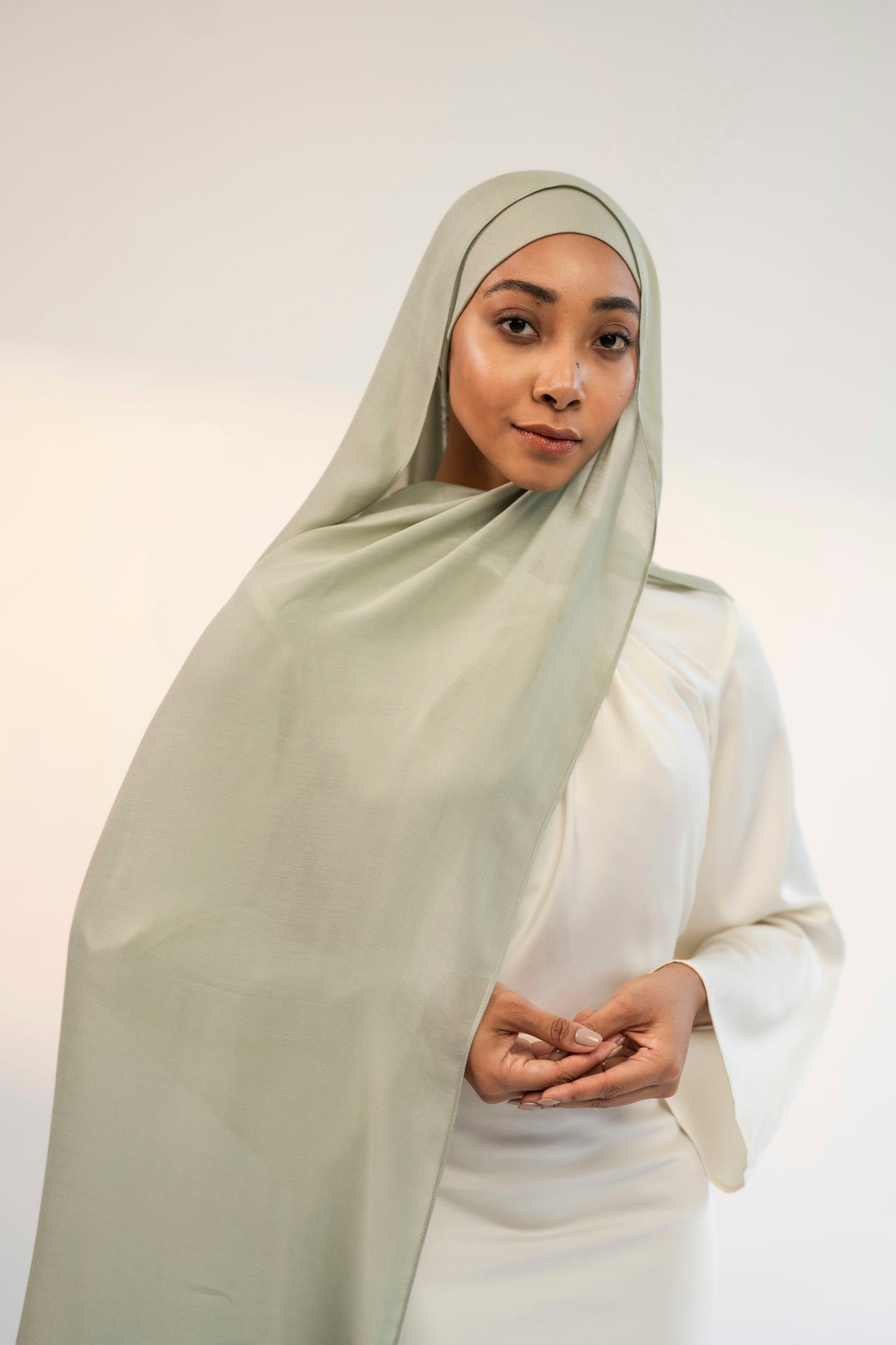 Woman wearing a light green hijab and white outfit against a plain background - sunlit mint