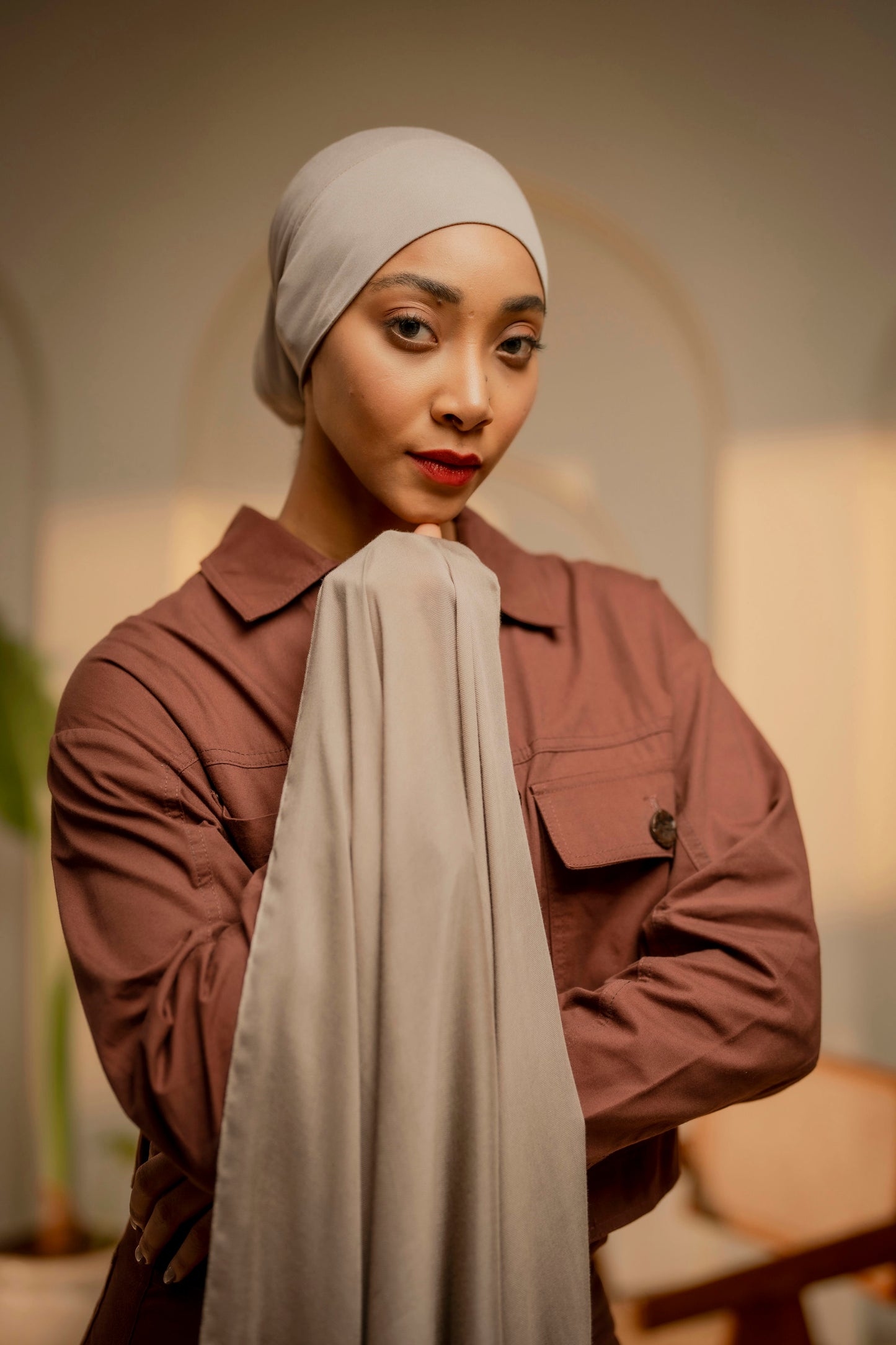 Woman wearing a beige hijab and brown jacket indoors - tan