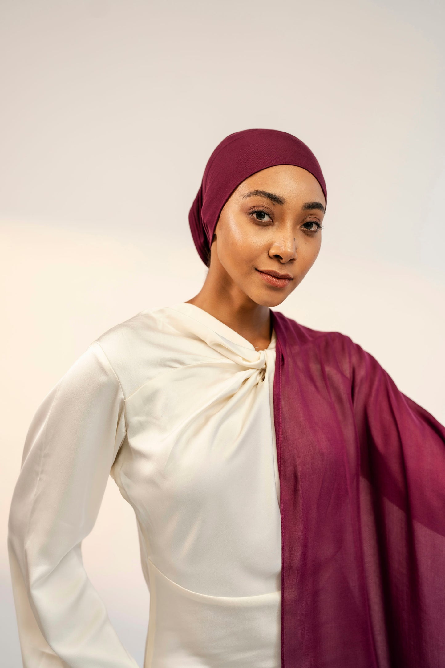 Woman wearing a white top and maroon headscarf and shawl against a plain background - wine