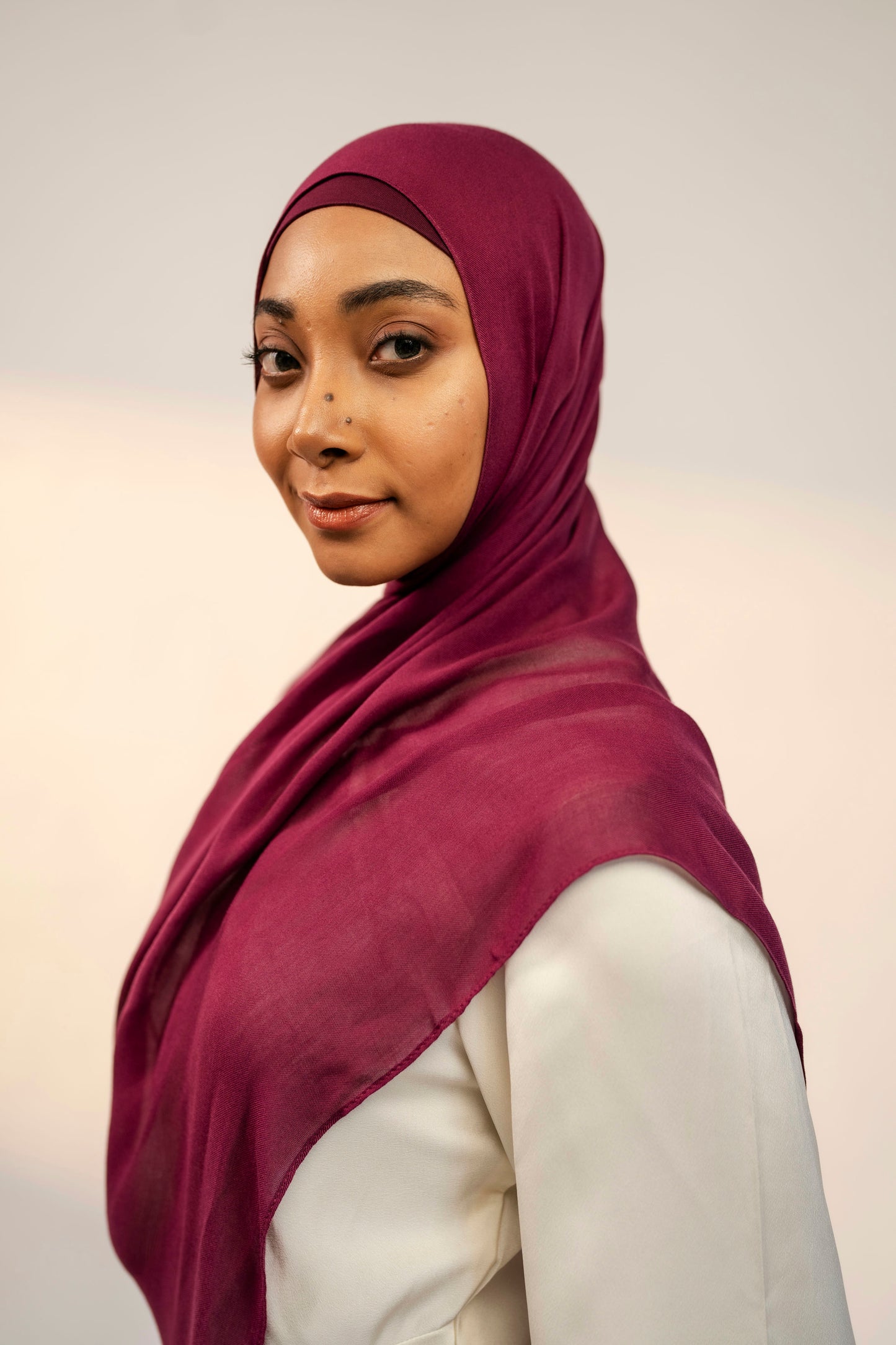Woman wearing a maroon hijab against a plain background - wine colour