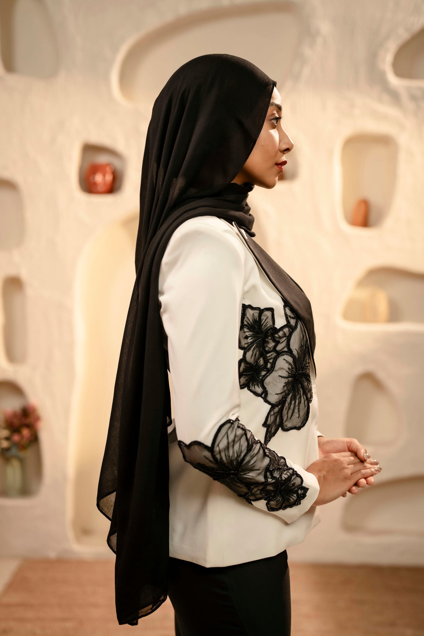 Woman wearing a black hijab and white blouse with black floral patterns in an indoor setting.
