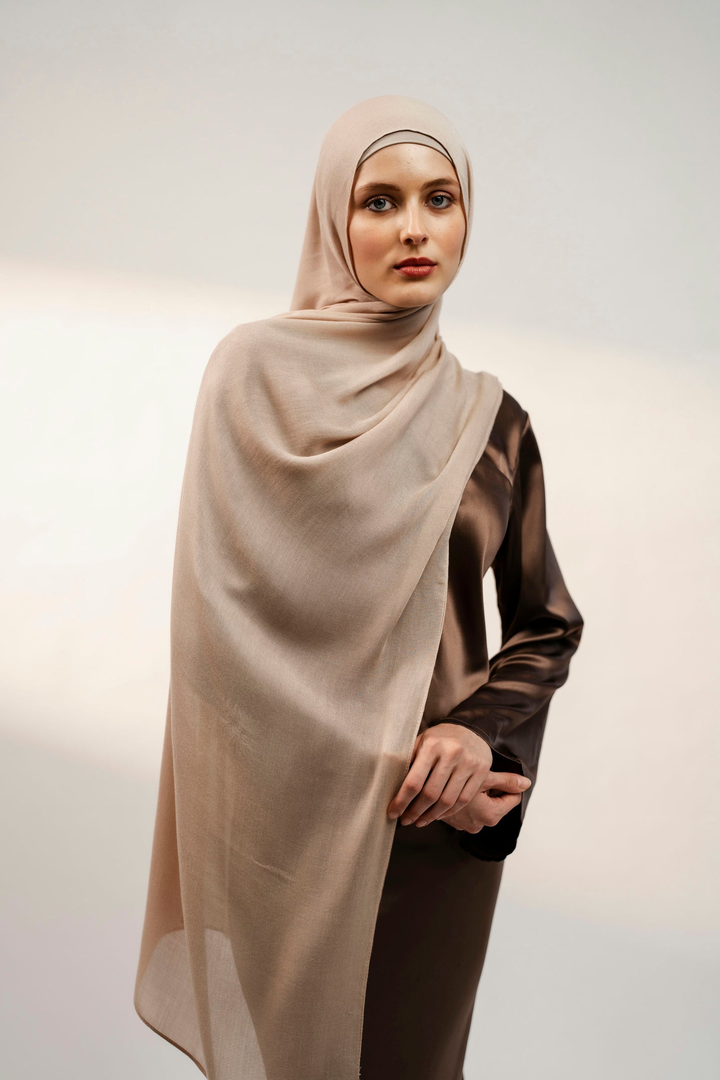 Woman wearing a beige hijab and brown outfit against a plain background - nude