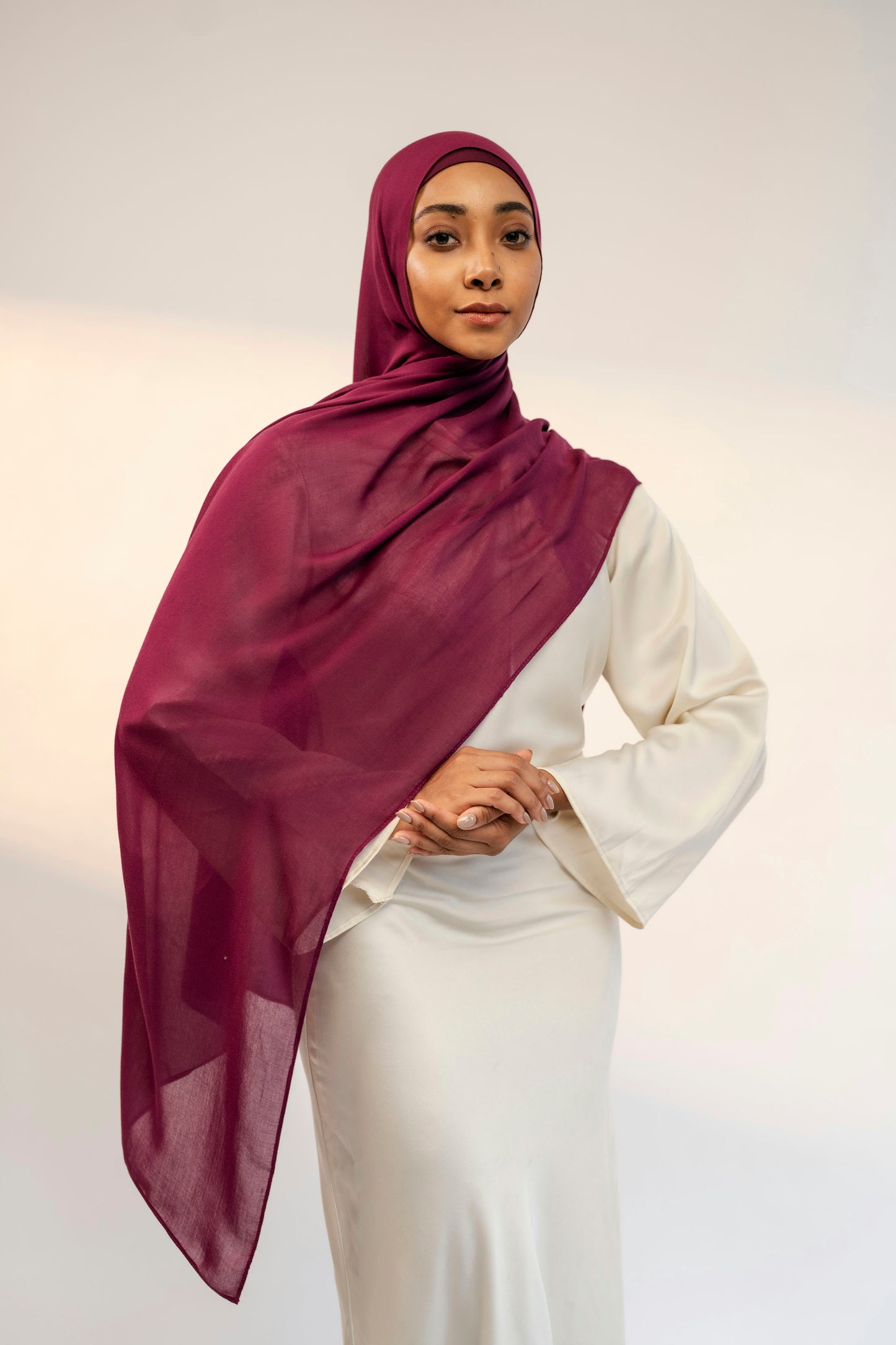 Woman wearing a burgundy hijab and white outfit against a plain background - wine