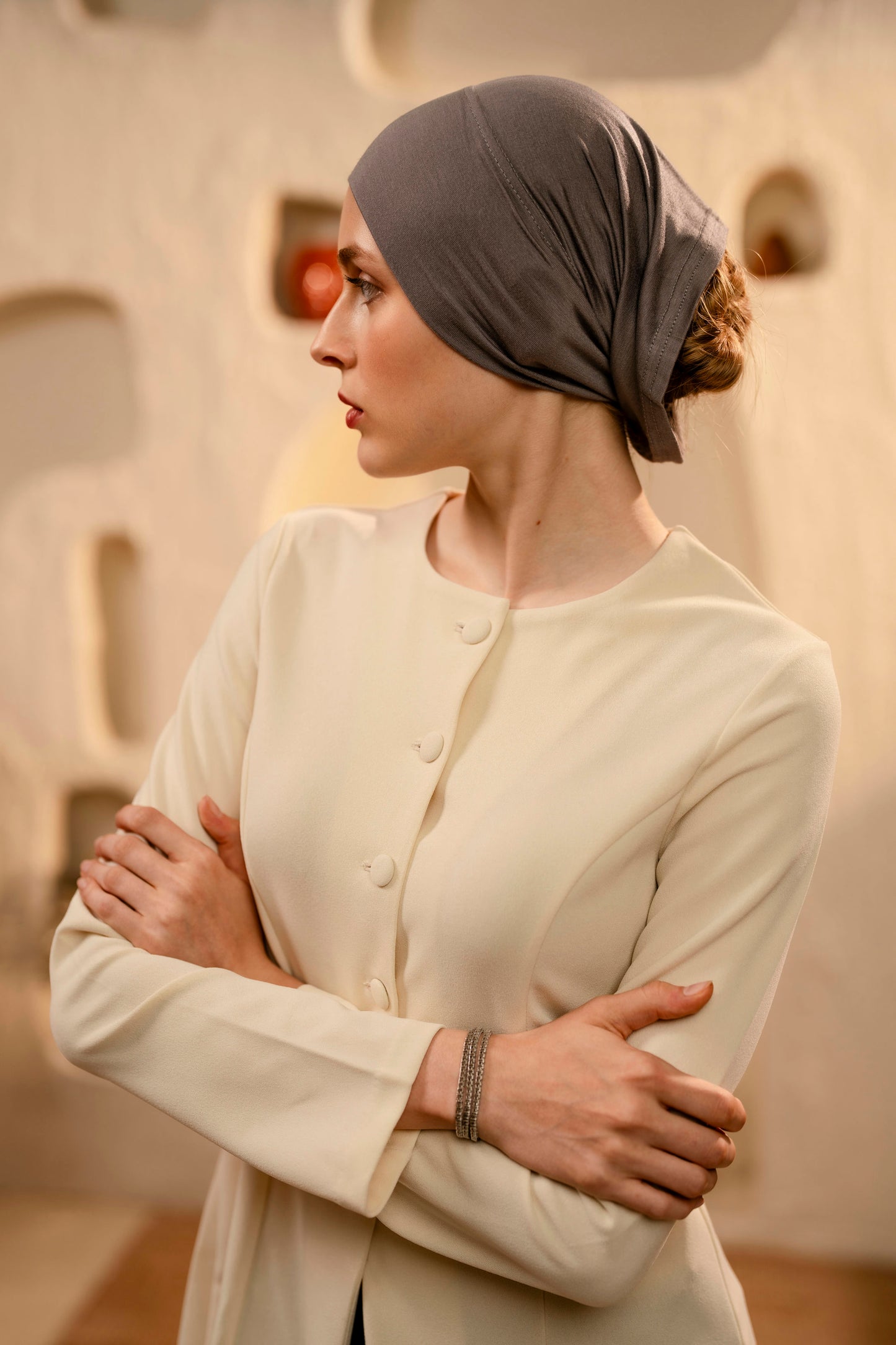 Woman wearing a gray headscarf and beige blouse against a neutral background - warm gray
