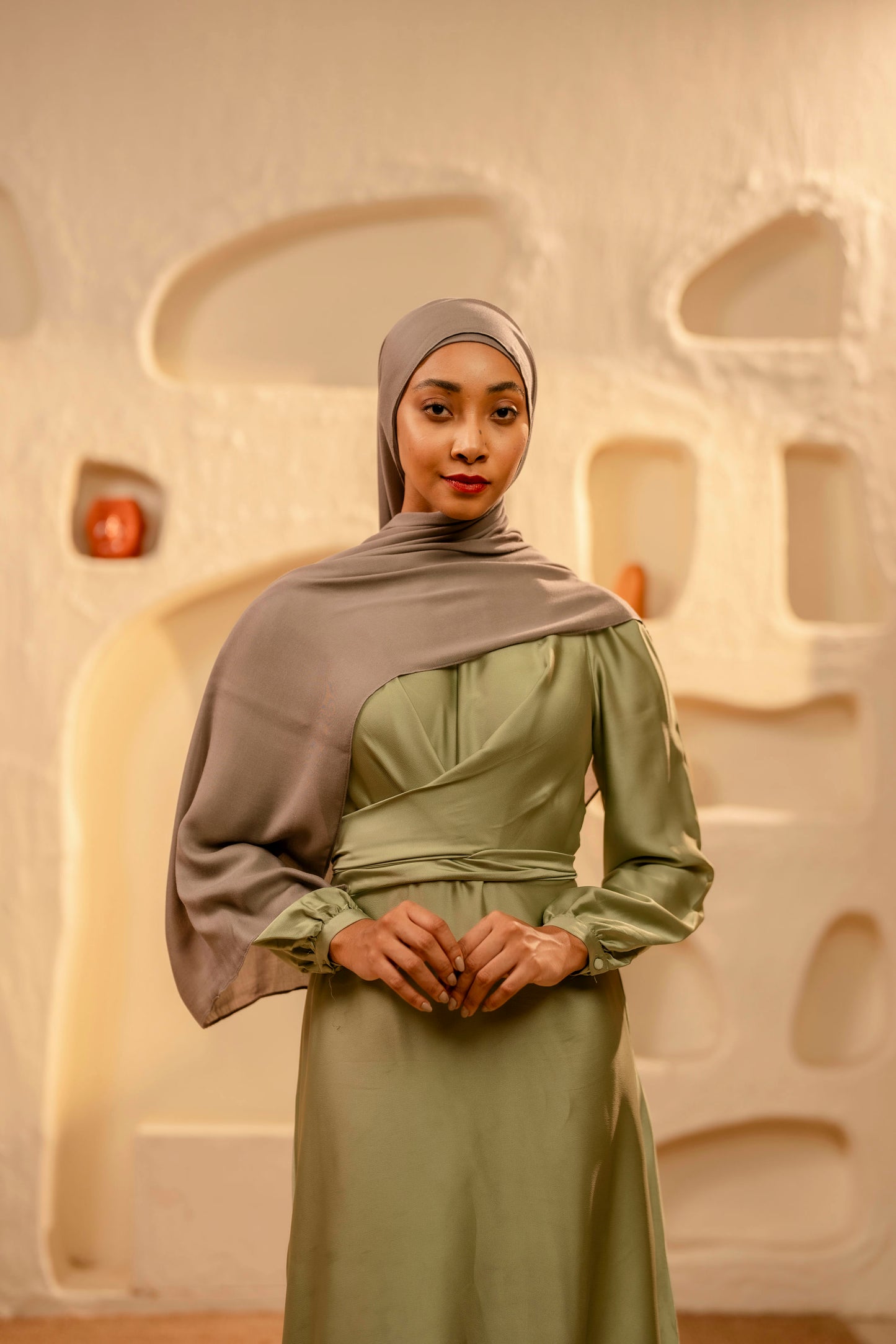 Woman wearing a green dress and gray hijab against an abstract beige background - khaki