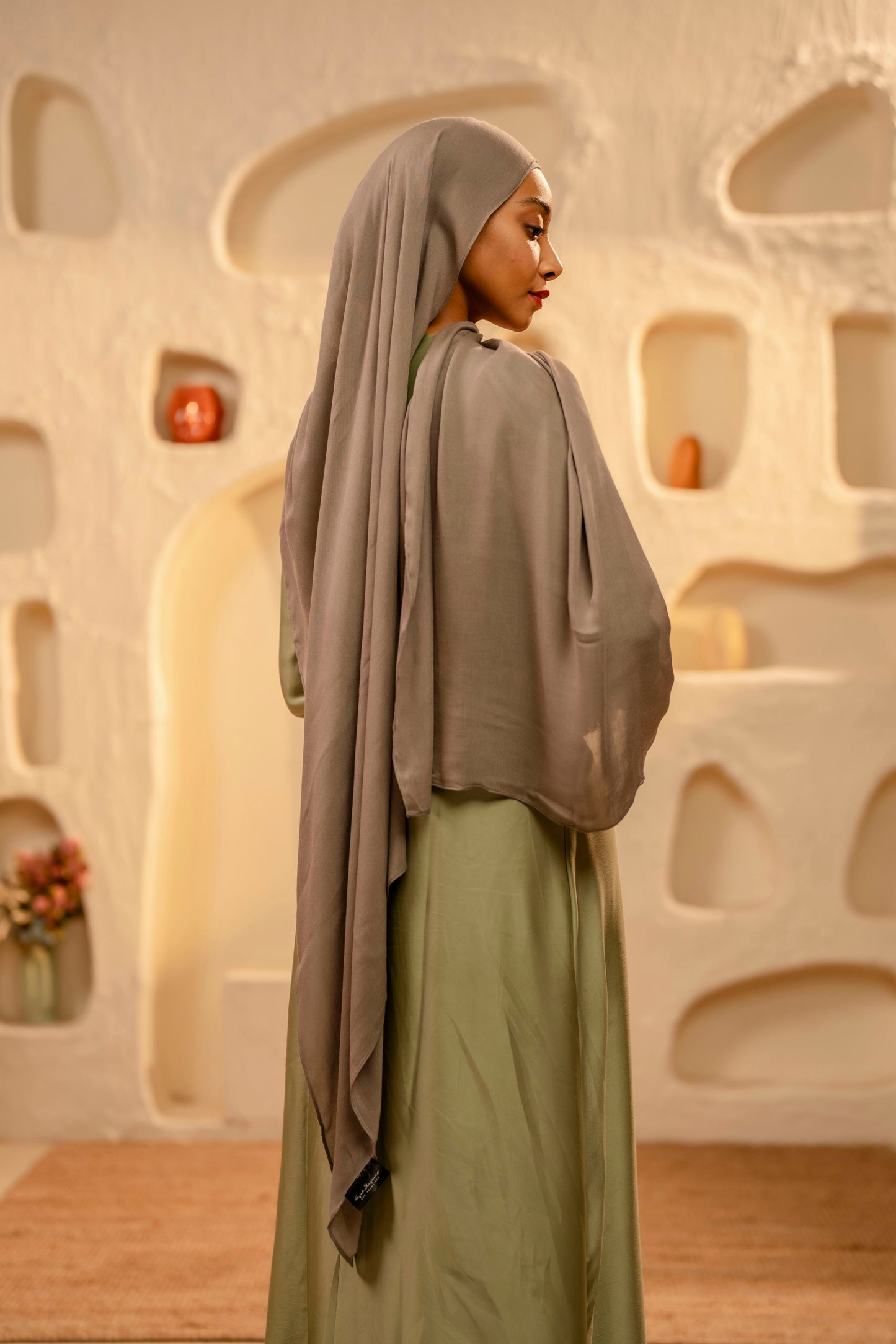 Woman wearing a hijab and green dress posing in front of an abstract wall - khaki