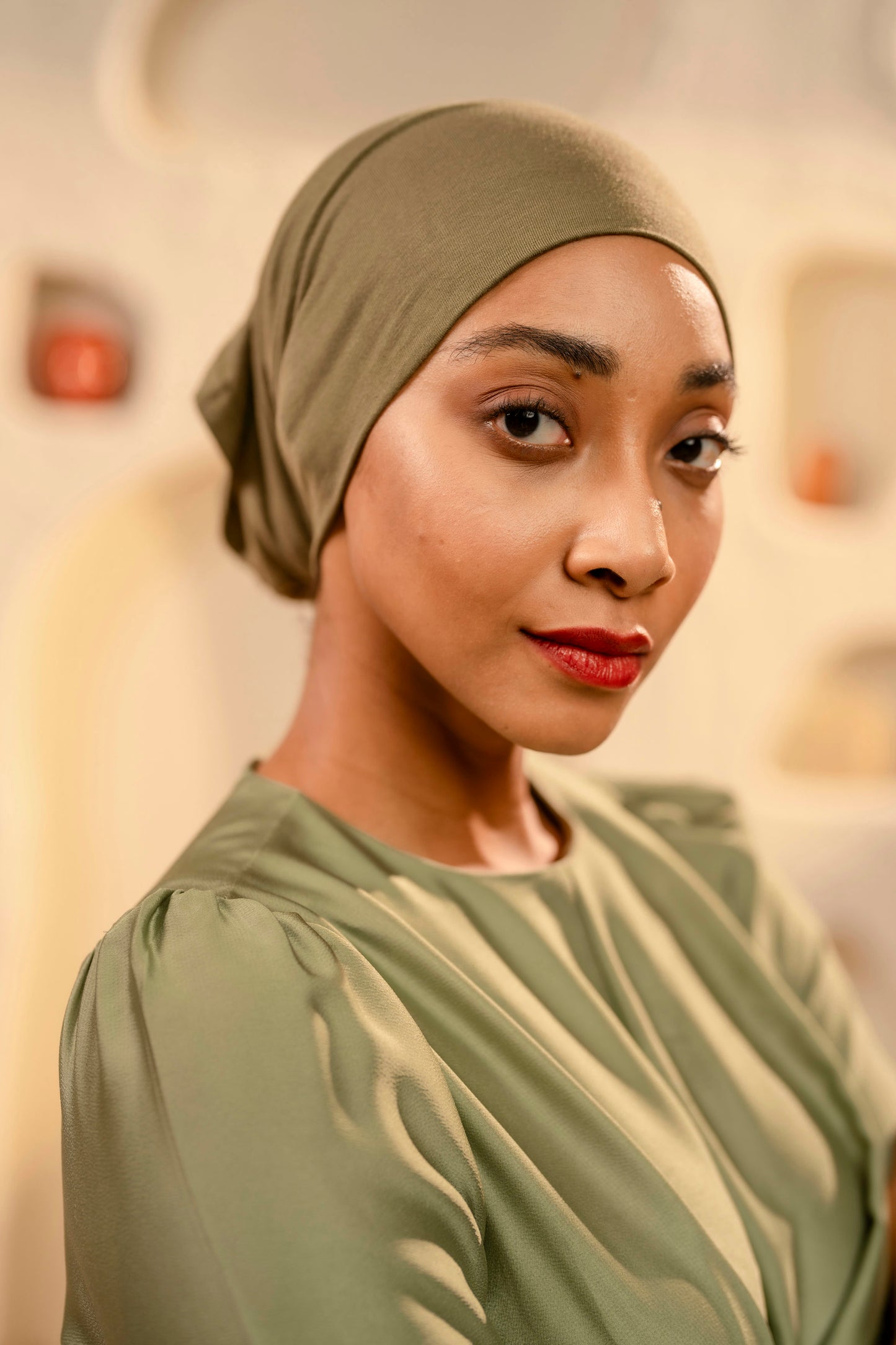 Woman wearing a olive green headscarf and dress against a blurred background