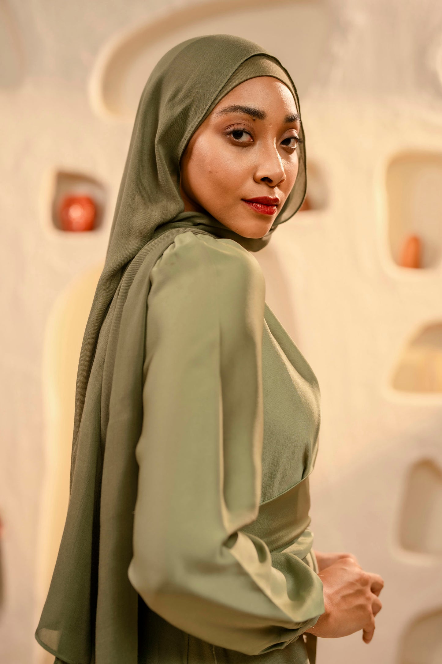 Woman wearing a green hijab and matching outfit in a neutral setting - olive green