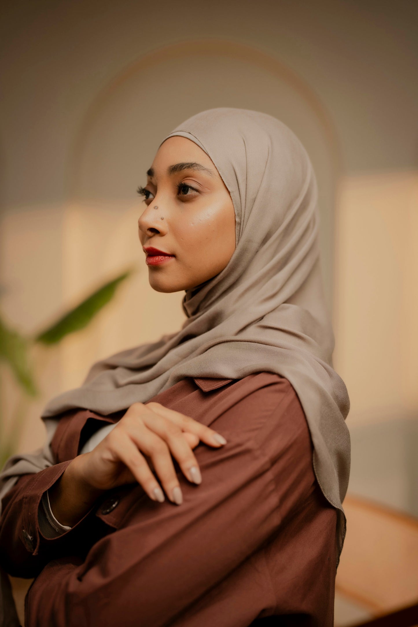 Woman wearing a beige hijab and brown top in an indoor setting - tan color
