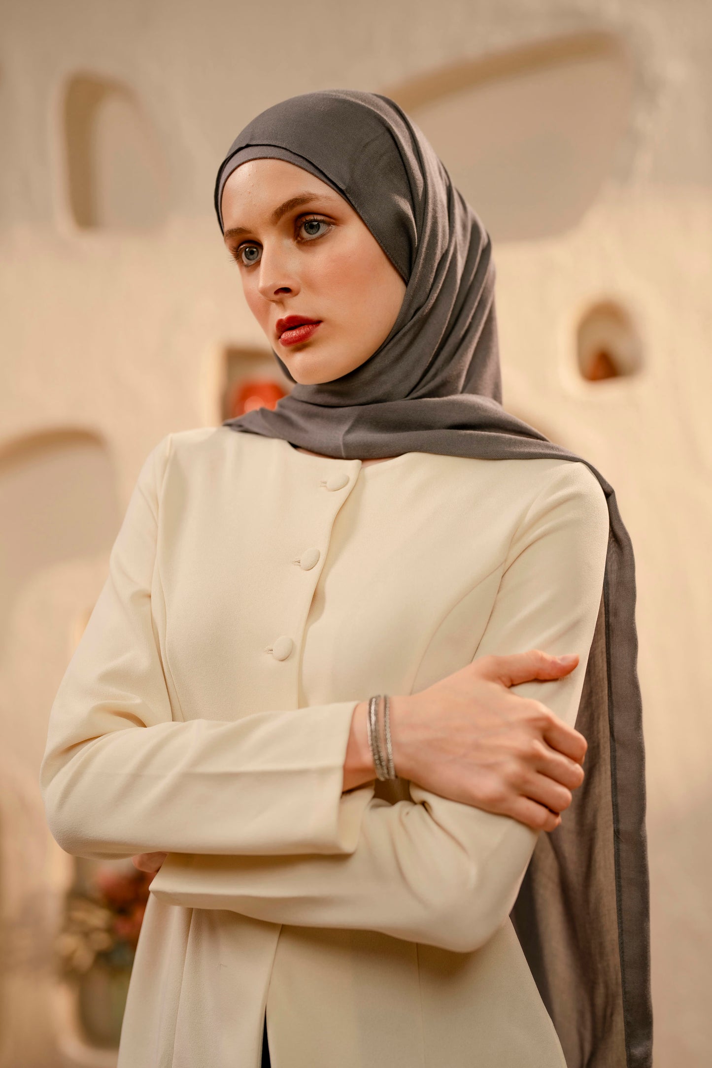 Woman wearing a warm gray hijab and cream outfit in an indoor setting