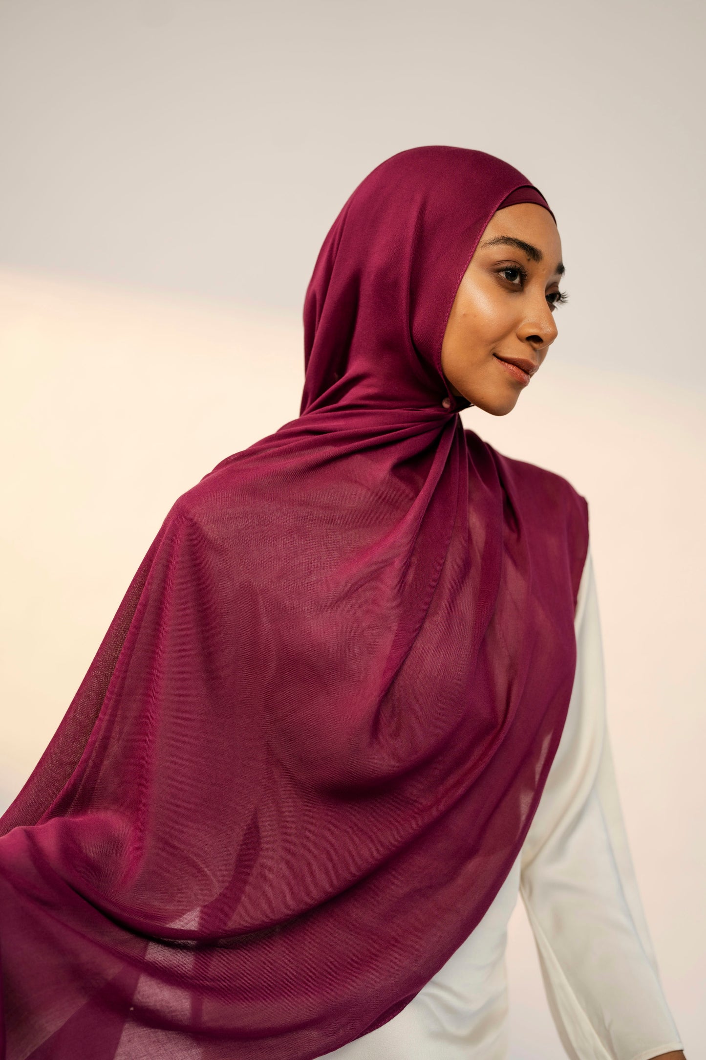 Woman wearing a burgundy hijab against a plain background - wine
