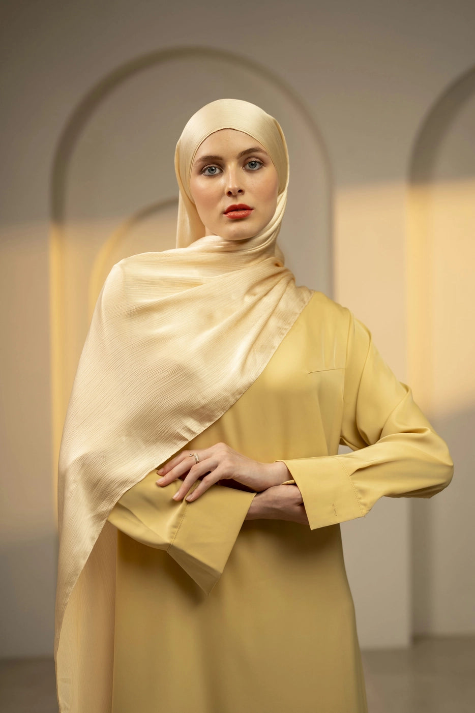 Woman wearing a yellow ivory hijab and dress in a softly lit room.