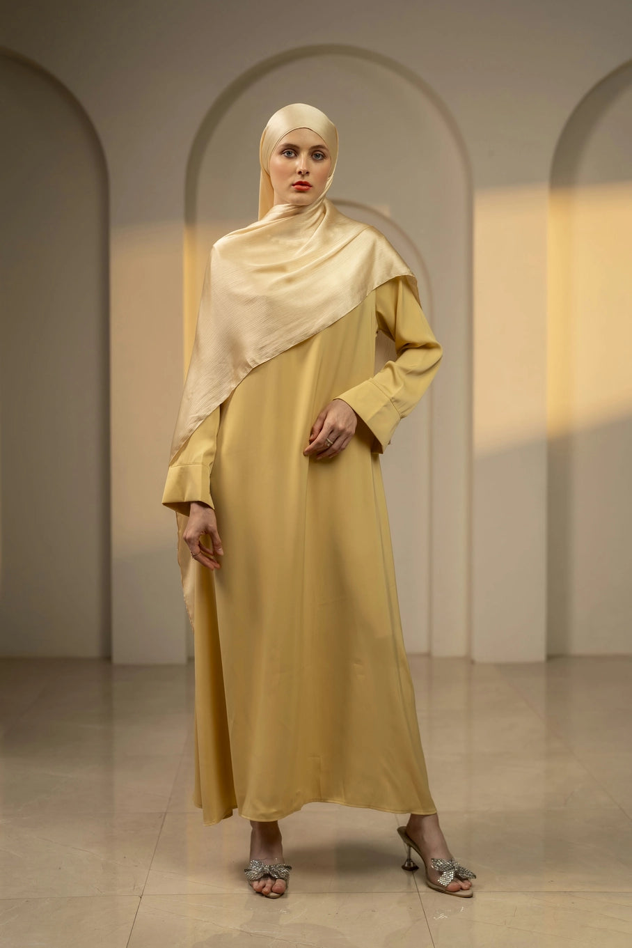 Woman wearing a yellow outfit with a matching ivory hijab in an elegant interior setting.